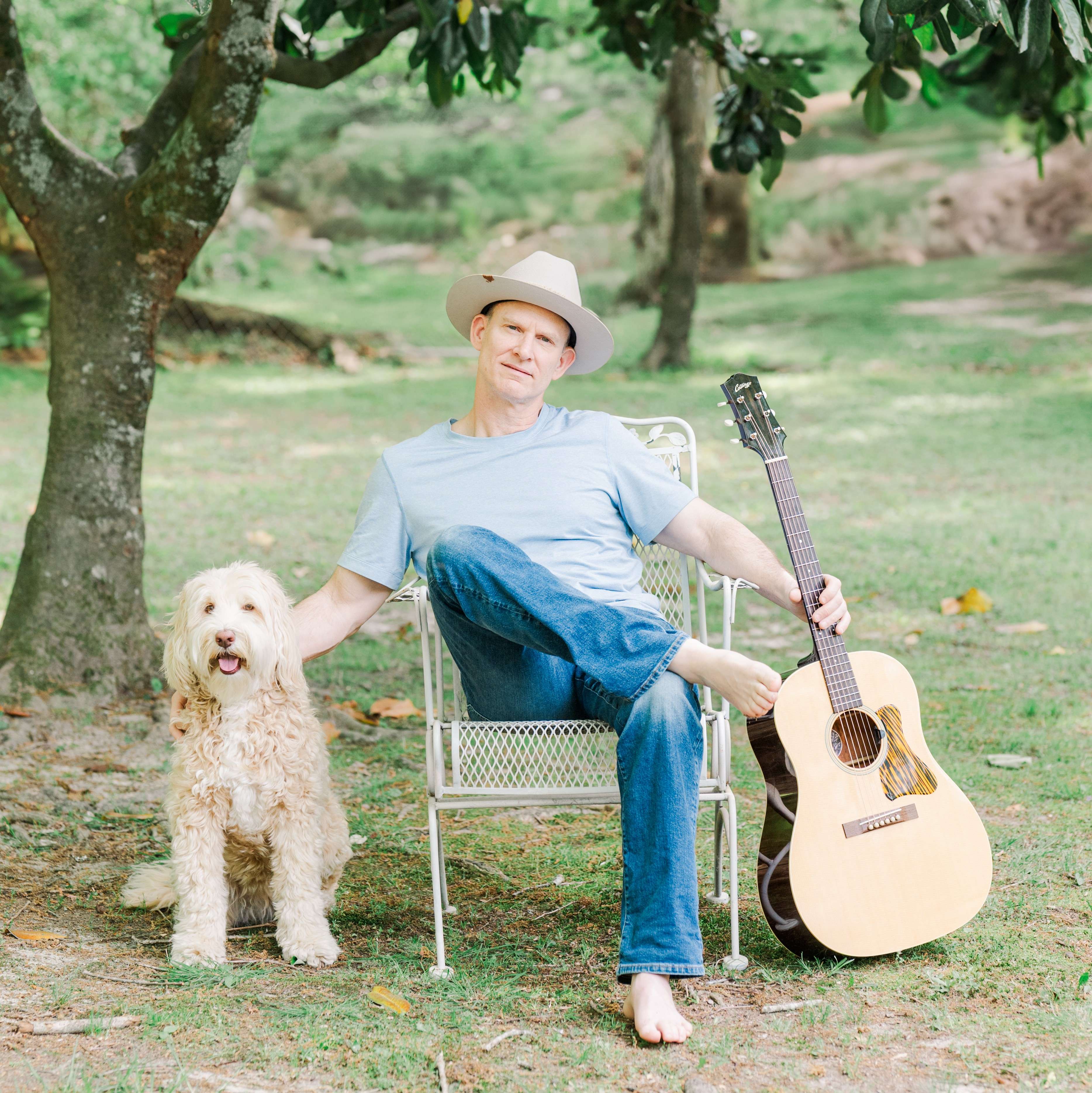 a man sitting on a chair with a guitar and a dog