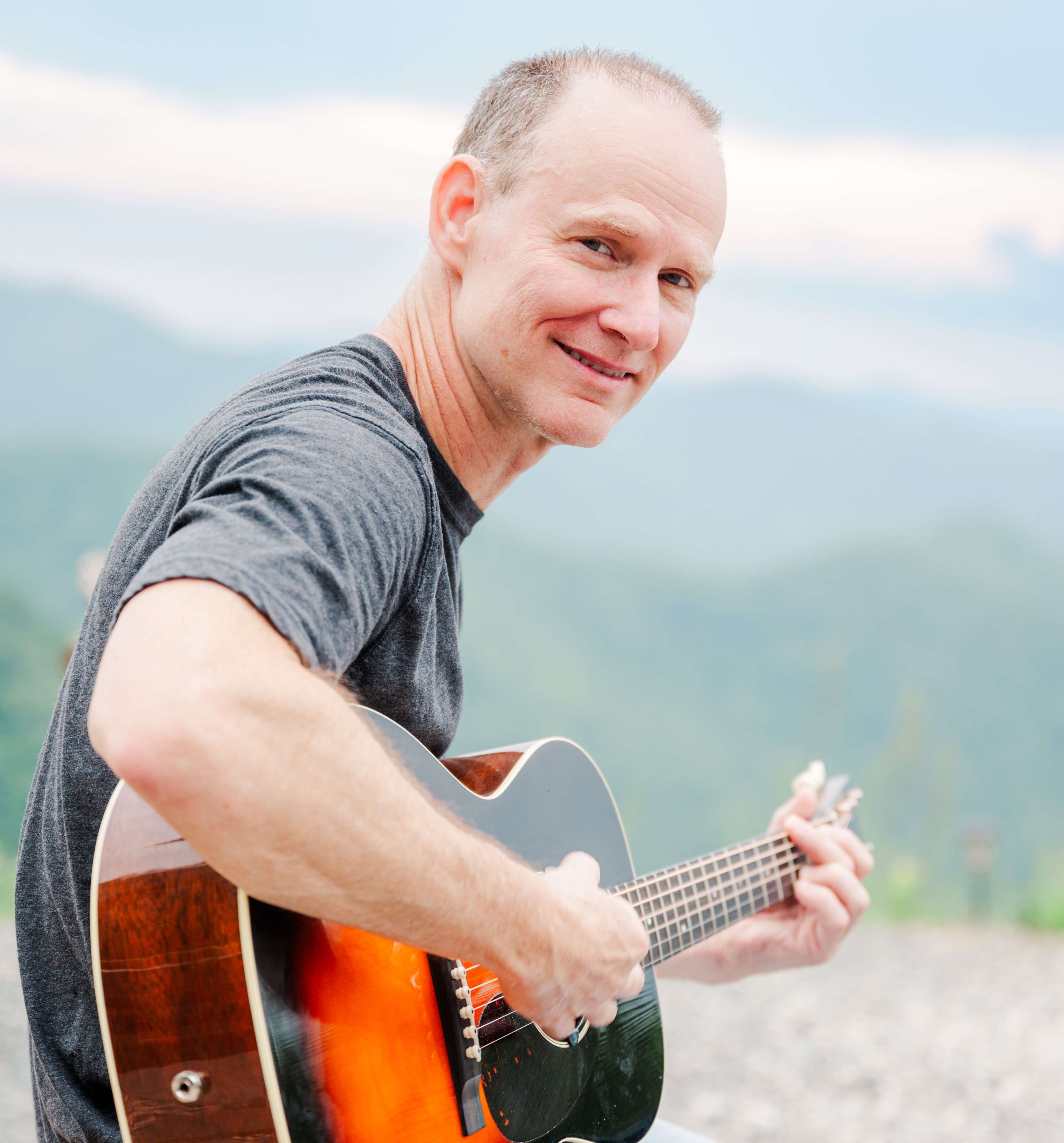 a man smiling while playing an acoustic guitar
