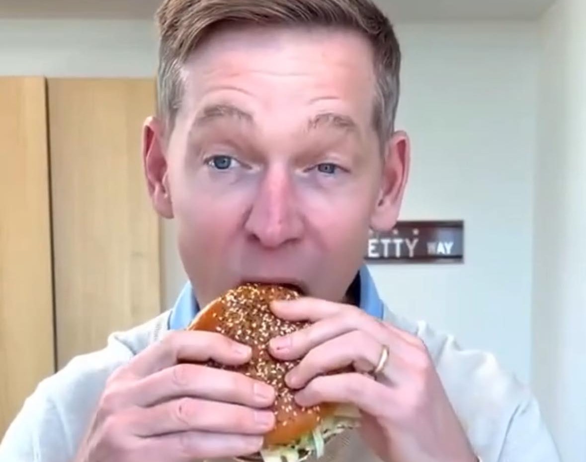 31) merch: a man is eating a large burger in front of a camera