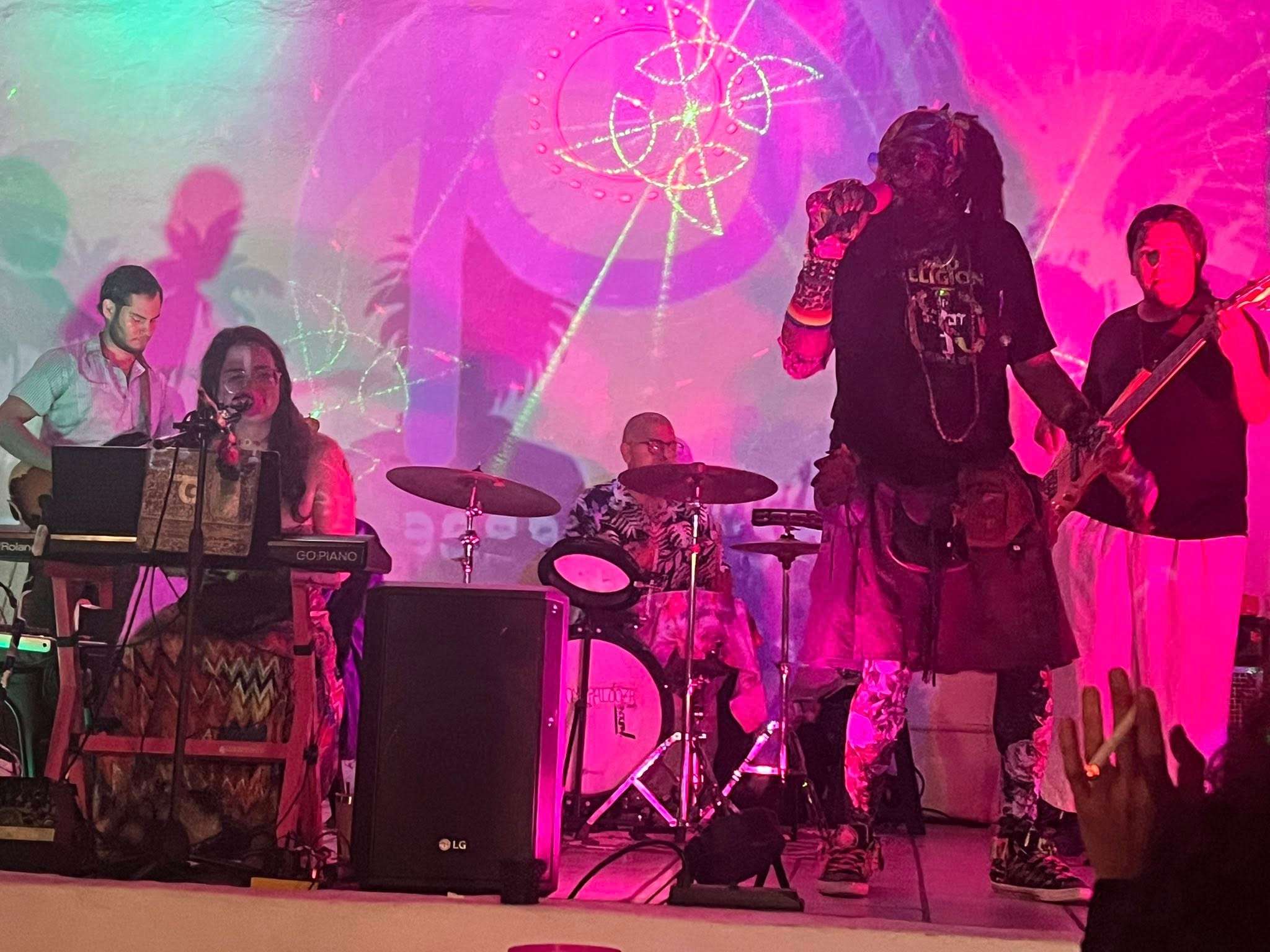 39) coded: a group of people playing music on stage in front of a pink background