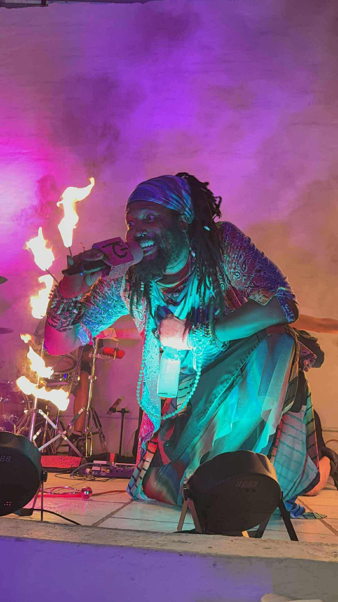 a man with dreadlocks sitting on a stage with fire in his hands