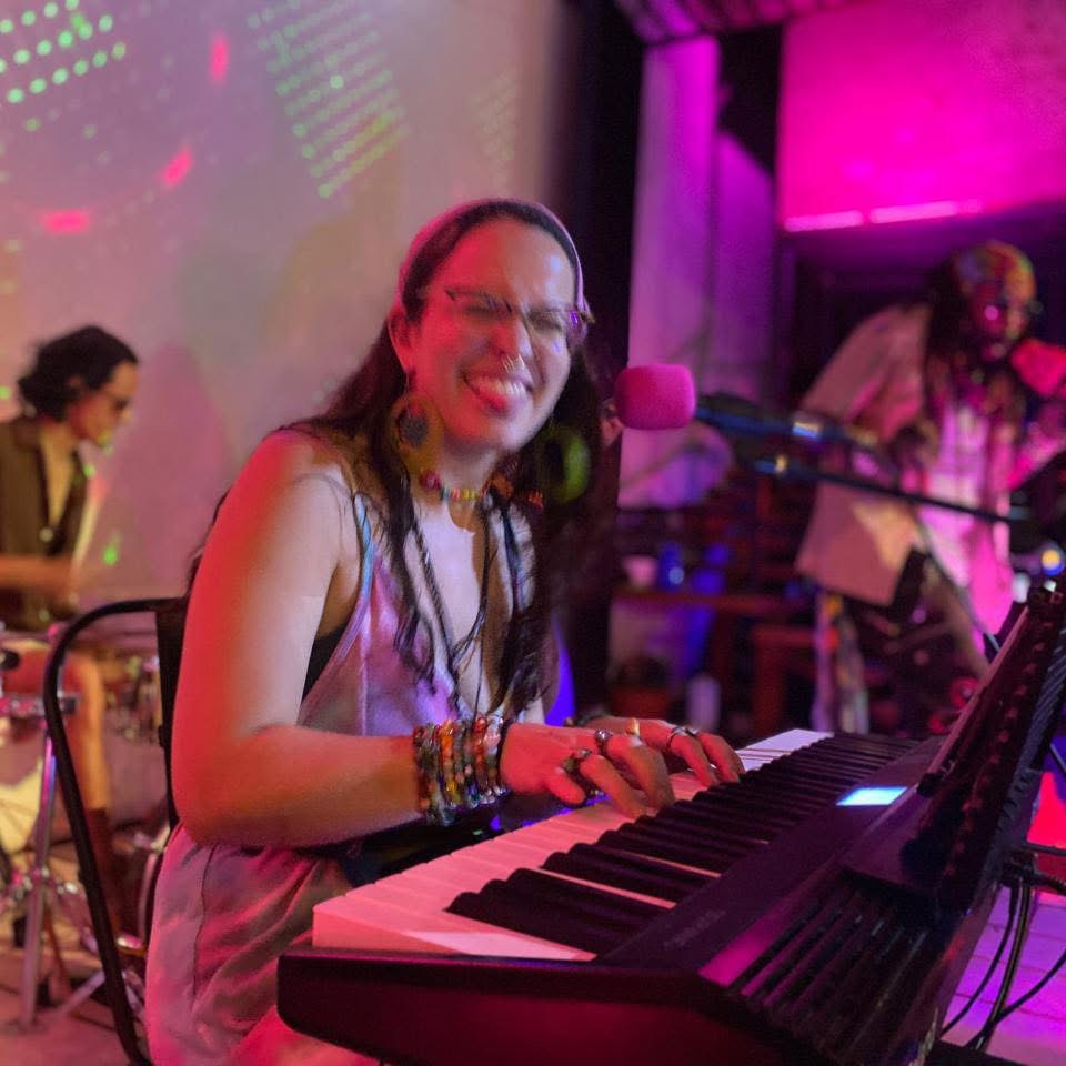 a woman playing a keyboard in front of a group of musicians