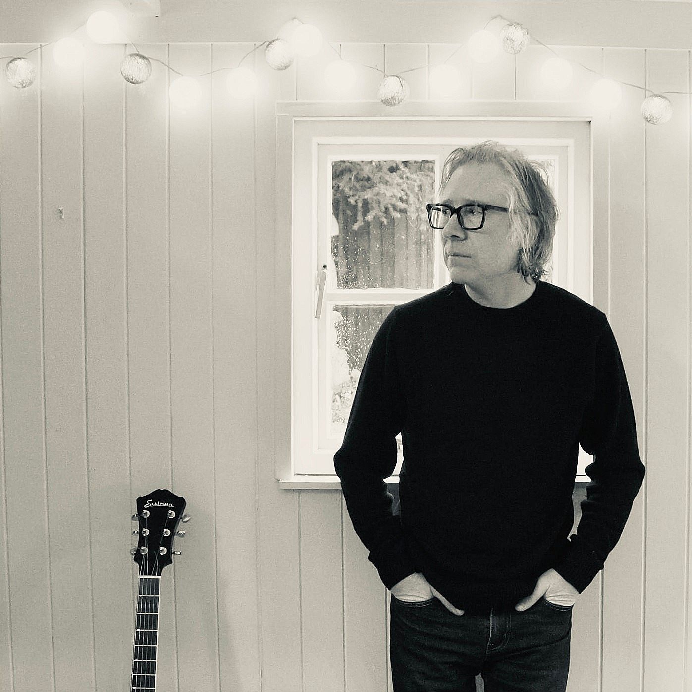 a man in glasses standing next to a guitar