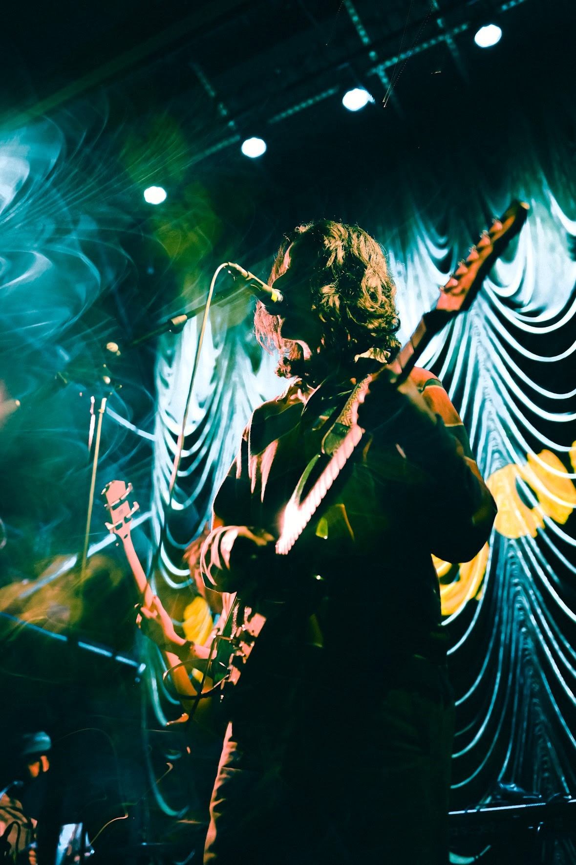 a man playing a guitar on stage in front of a curtain
