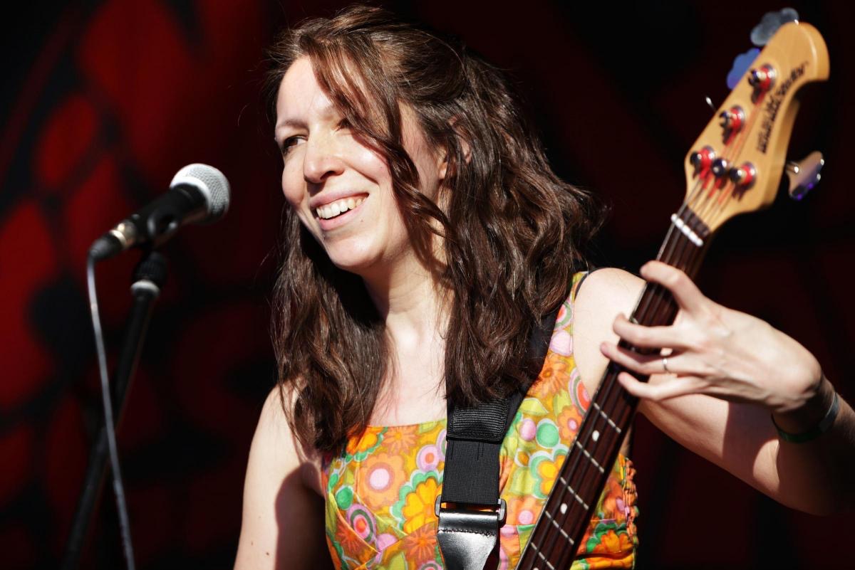 a woman smiling while holding a bass guitar