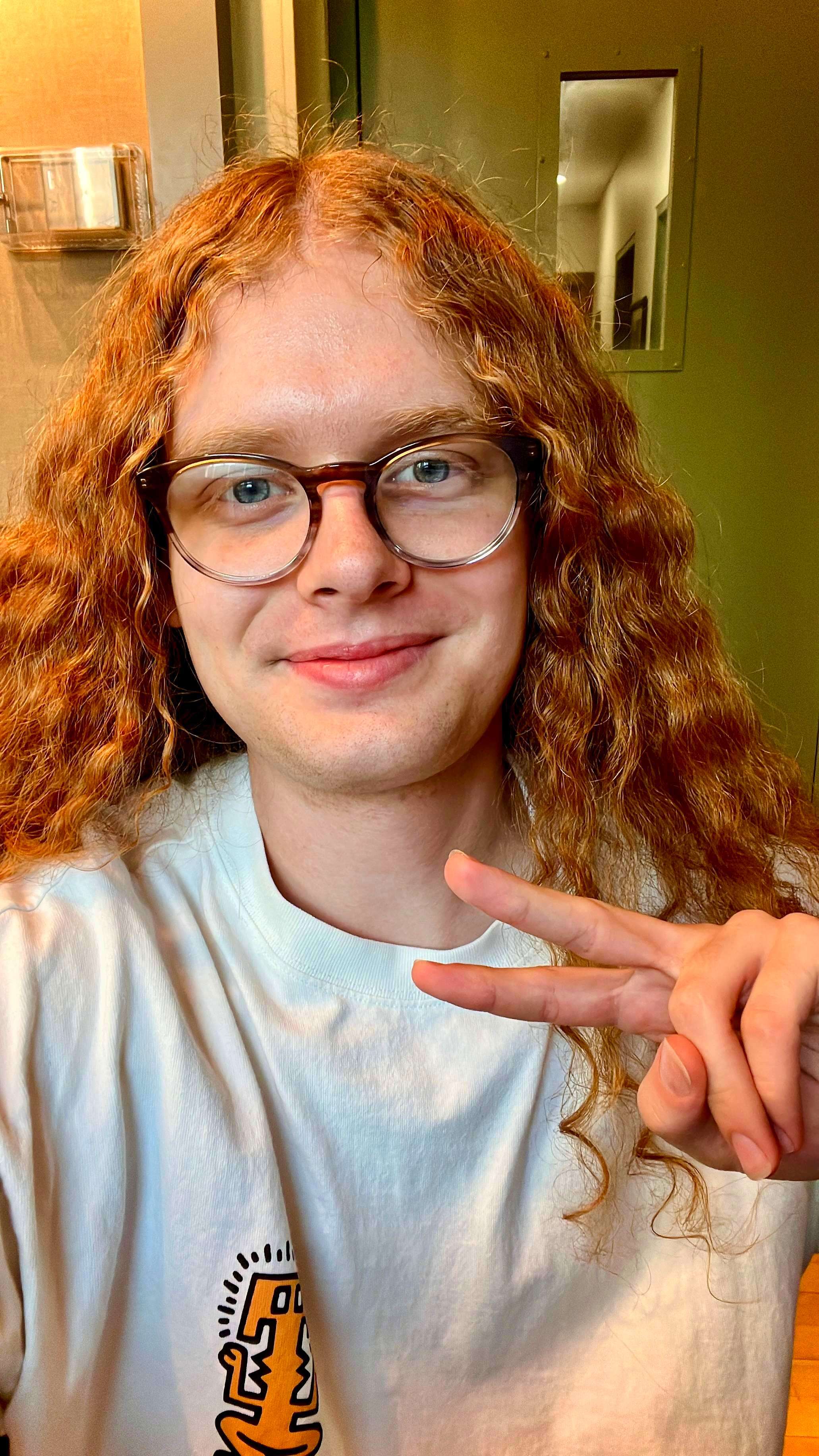 a young man with red curly hair making a peace sign