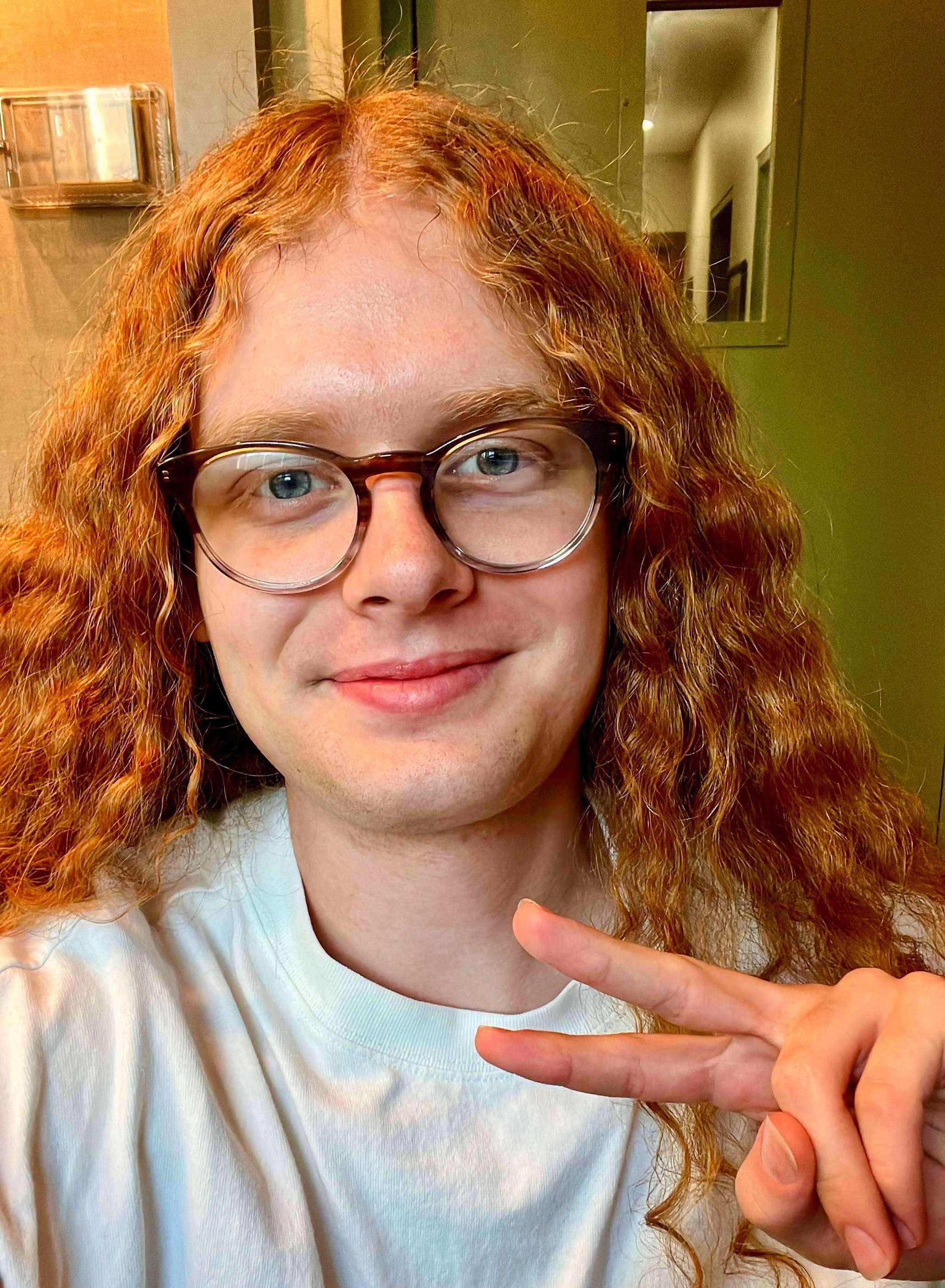 a man with red curly hair making a peace sign