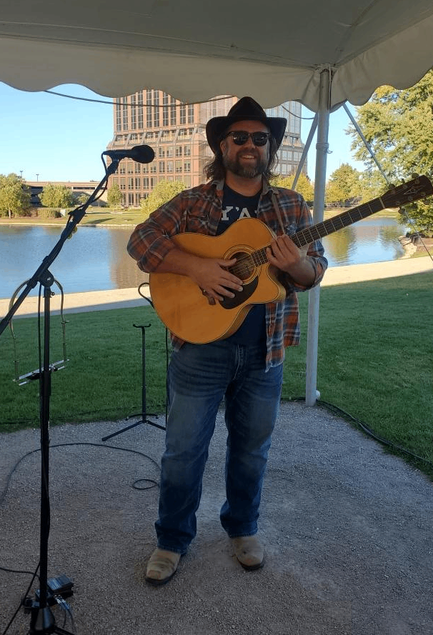 a man playing an acoustic guitar in front of a lake