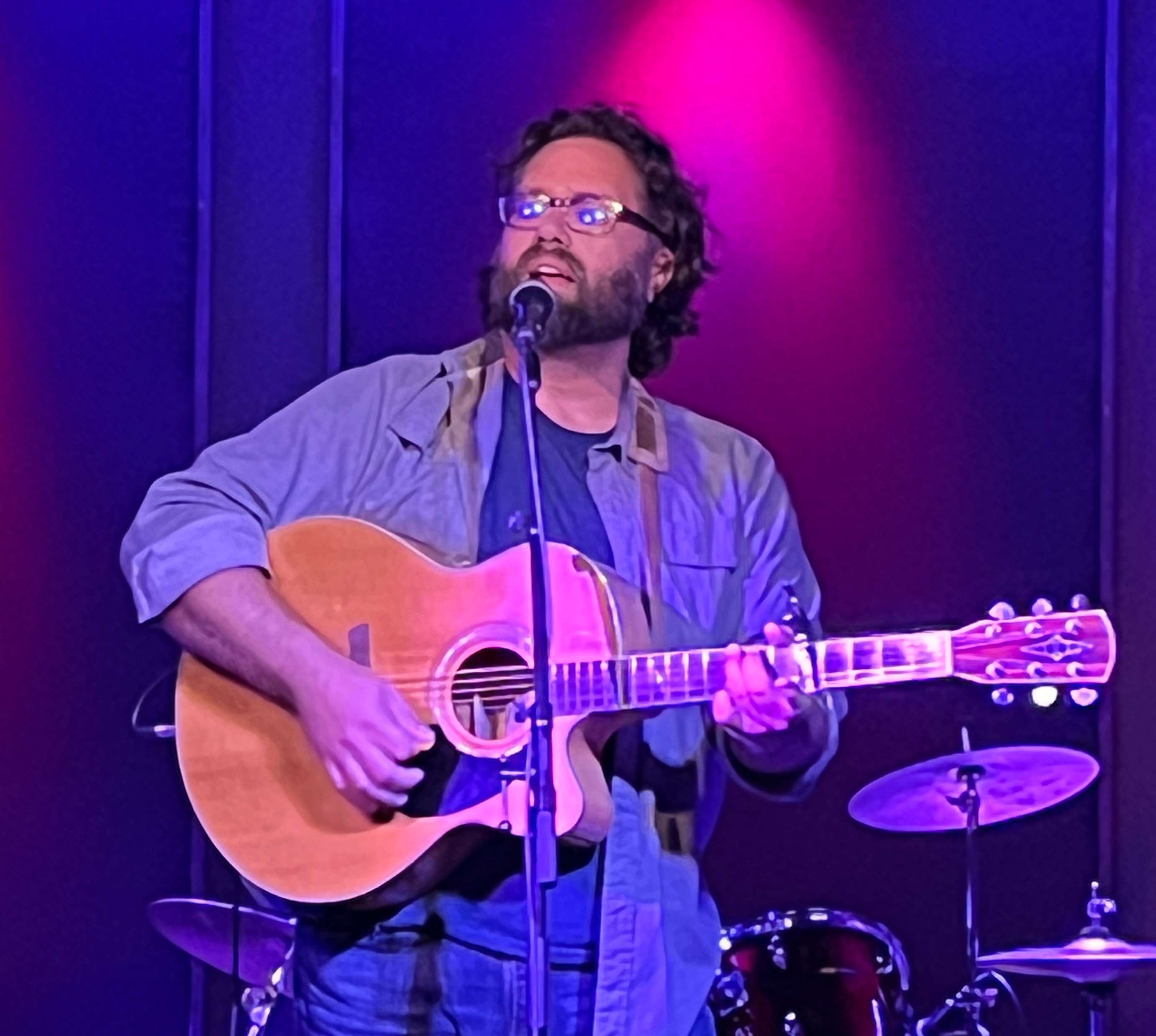 a man holding an acoustic guitar in front of a microphone
