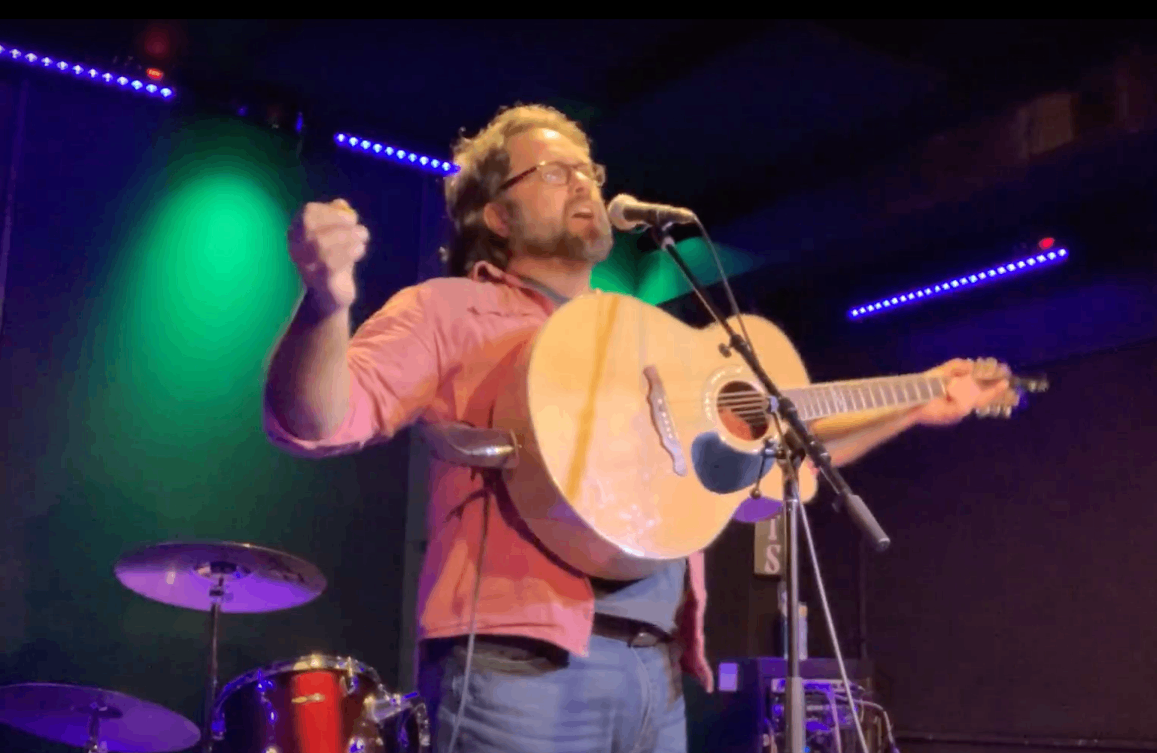 a man singing into a microphone while holding an acoustic guitar