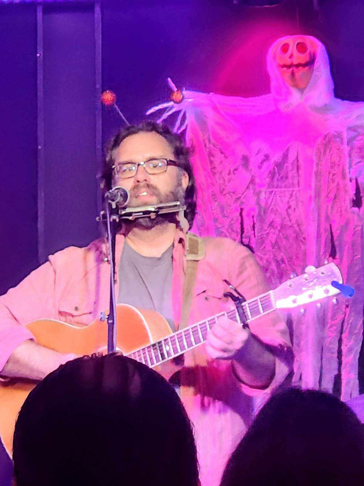 a man playing an acoustic guitar in front of a skeleton