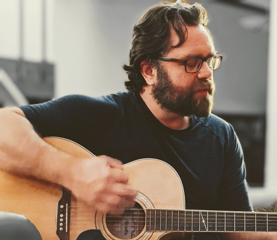 a man with glasses playing an acoustic guitar