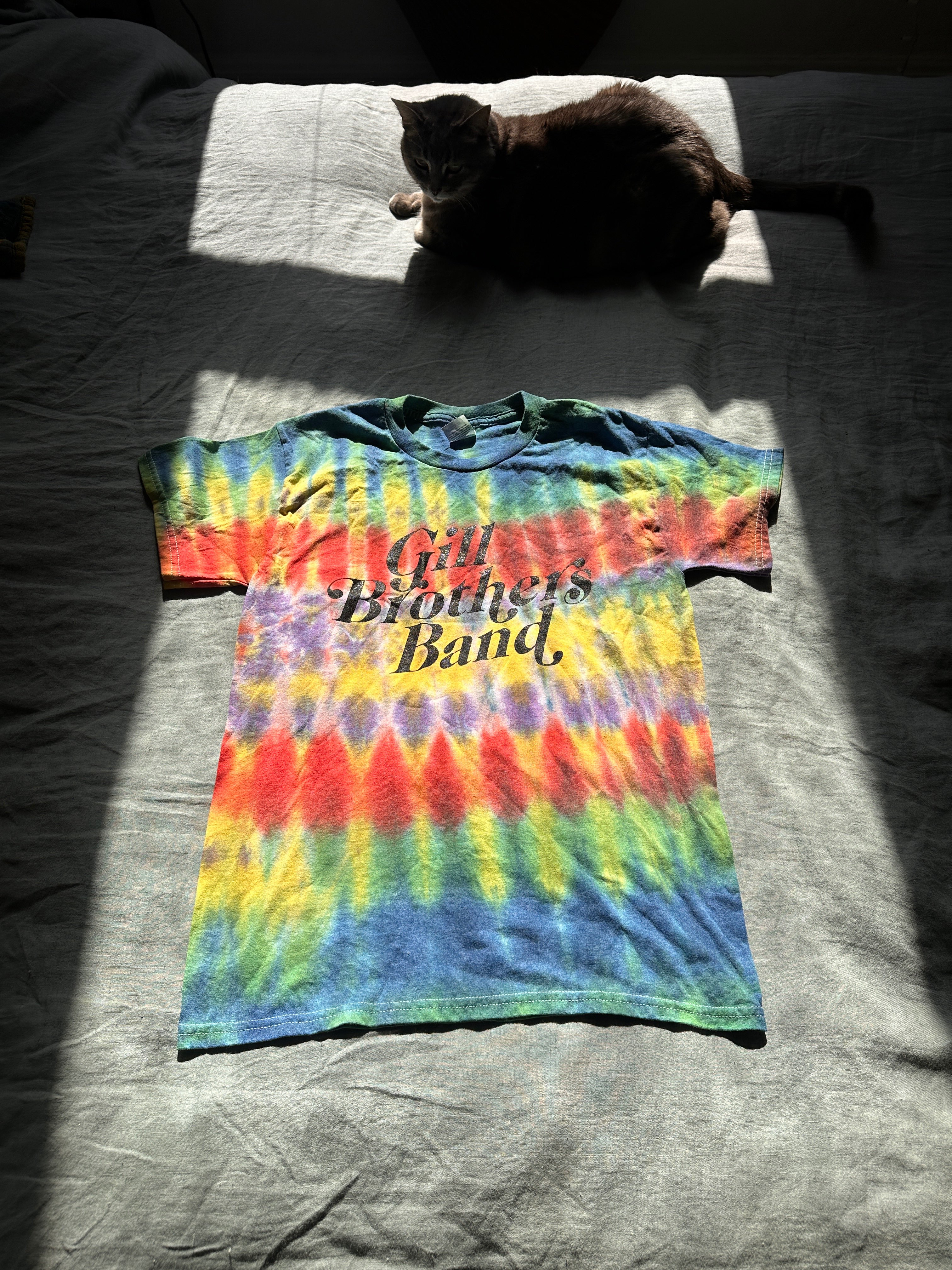 a cat is laying on a bed with a tie dye t - shirt