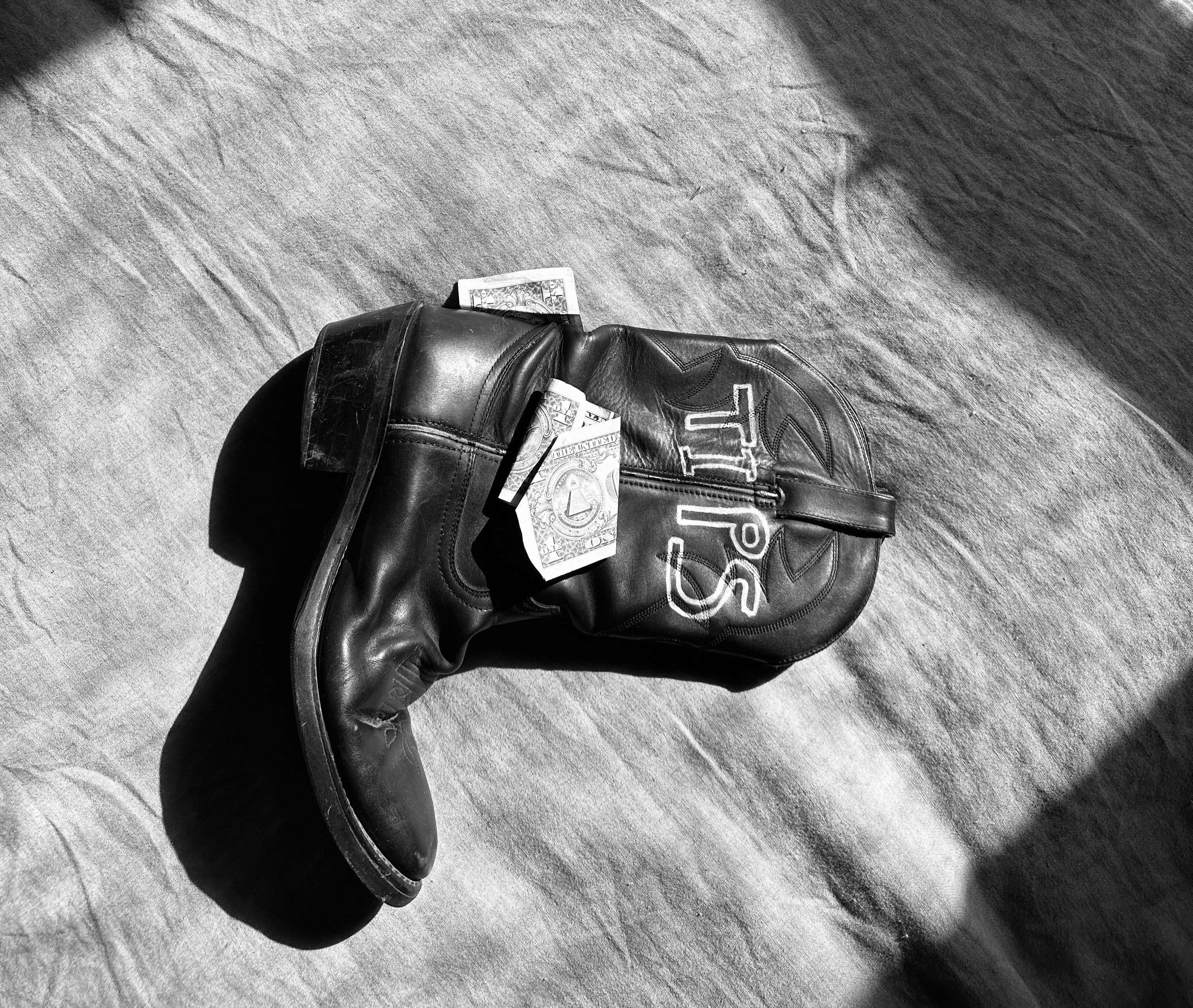 a black and white photo of a cowboy boot with money on it