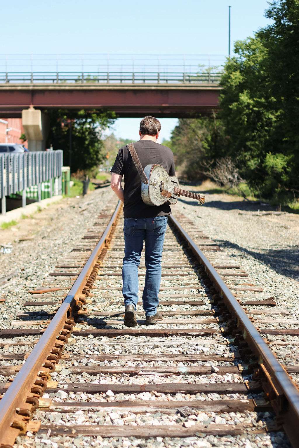 a man walking on railroad tracks with a guitar