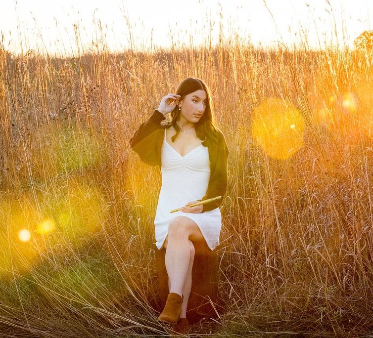 a woman in a white dress sitting in tall grass at sunset