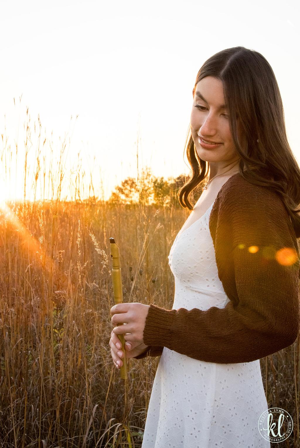 a woman in a white dress standing in tall grass at sunset
