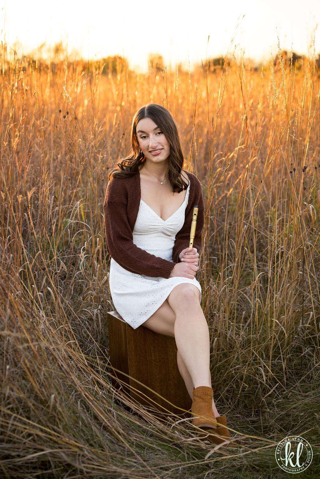 a young woman sitting on a wooden box in tall grass