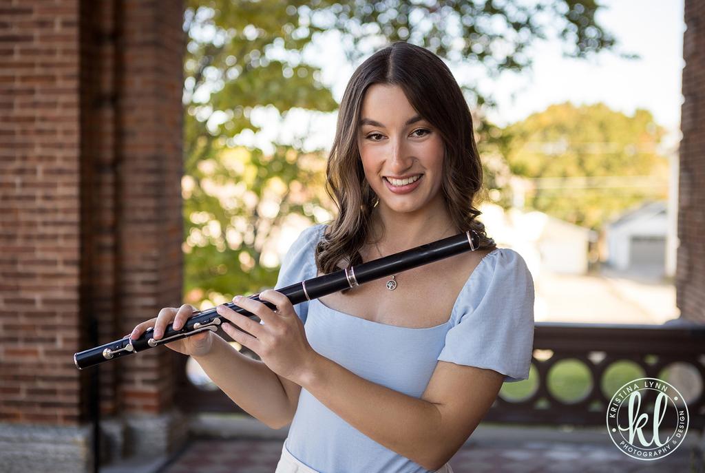 a young woman holding a flute in front of a brick building