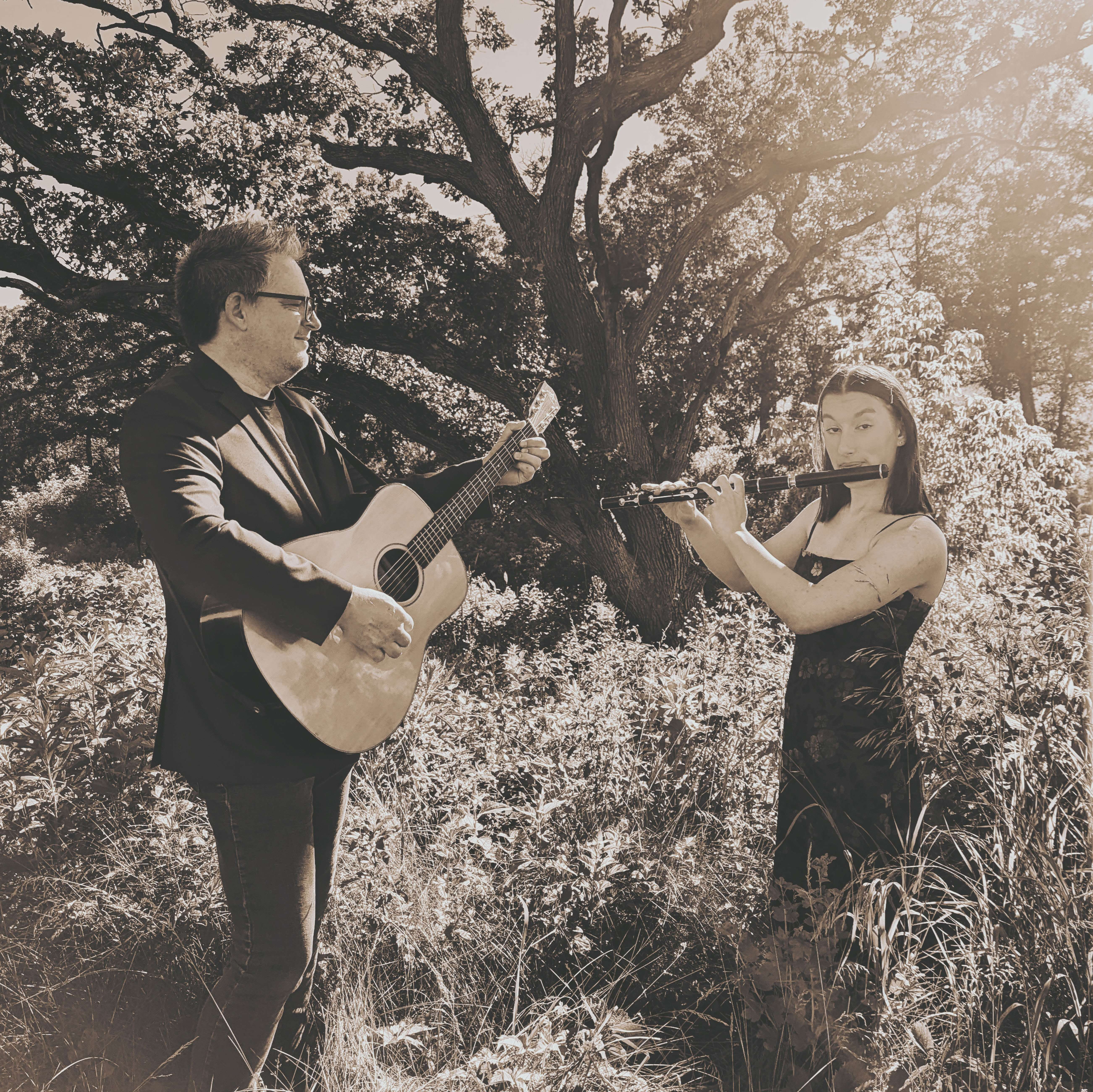 a man and a woman standing in a field with an acoustic guitar