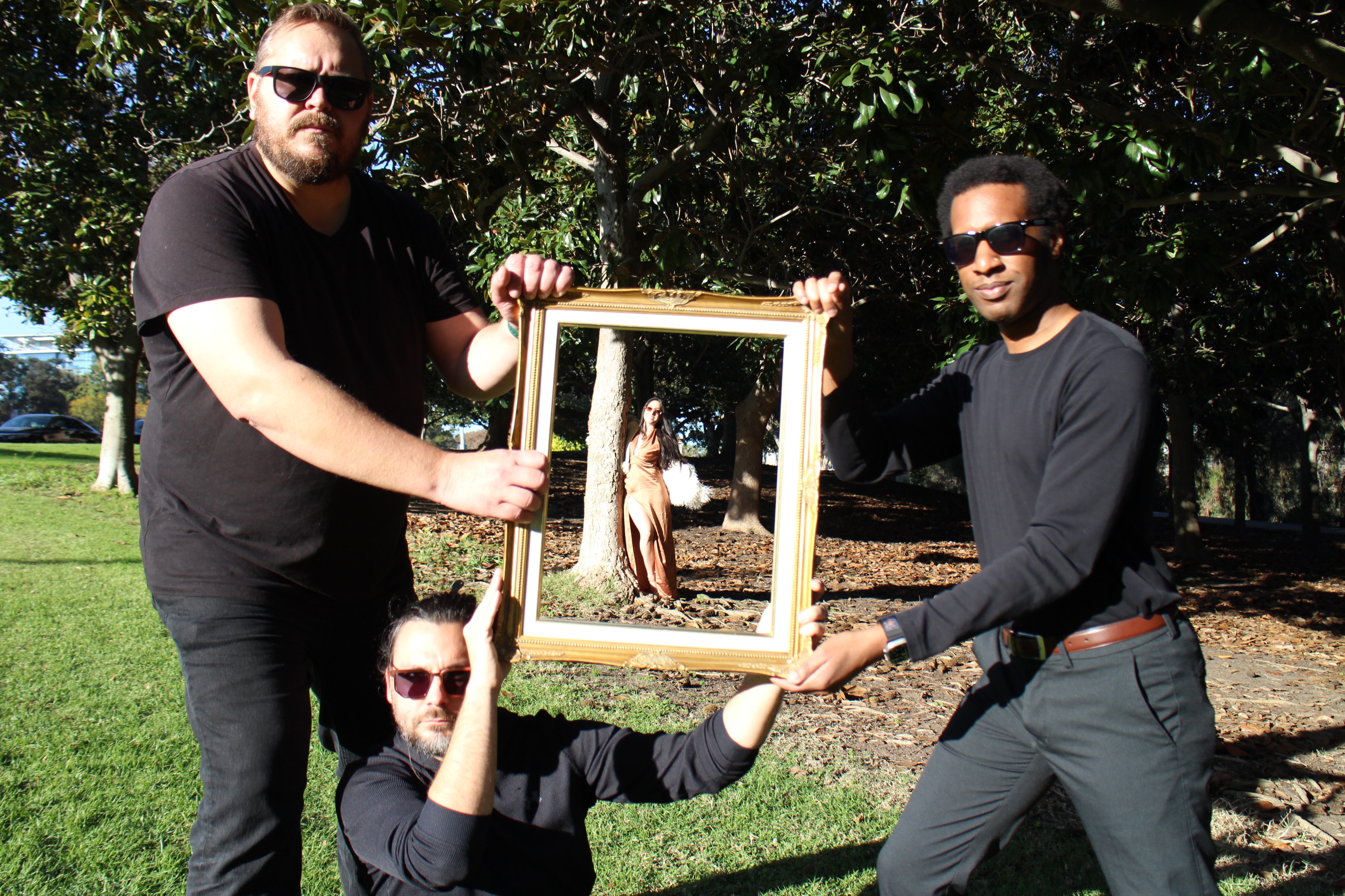 three men holding up a picture frame in a park