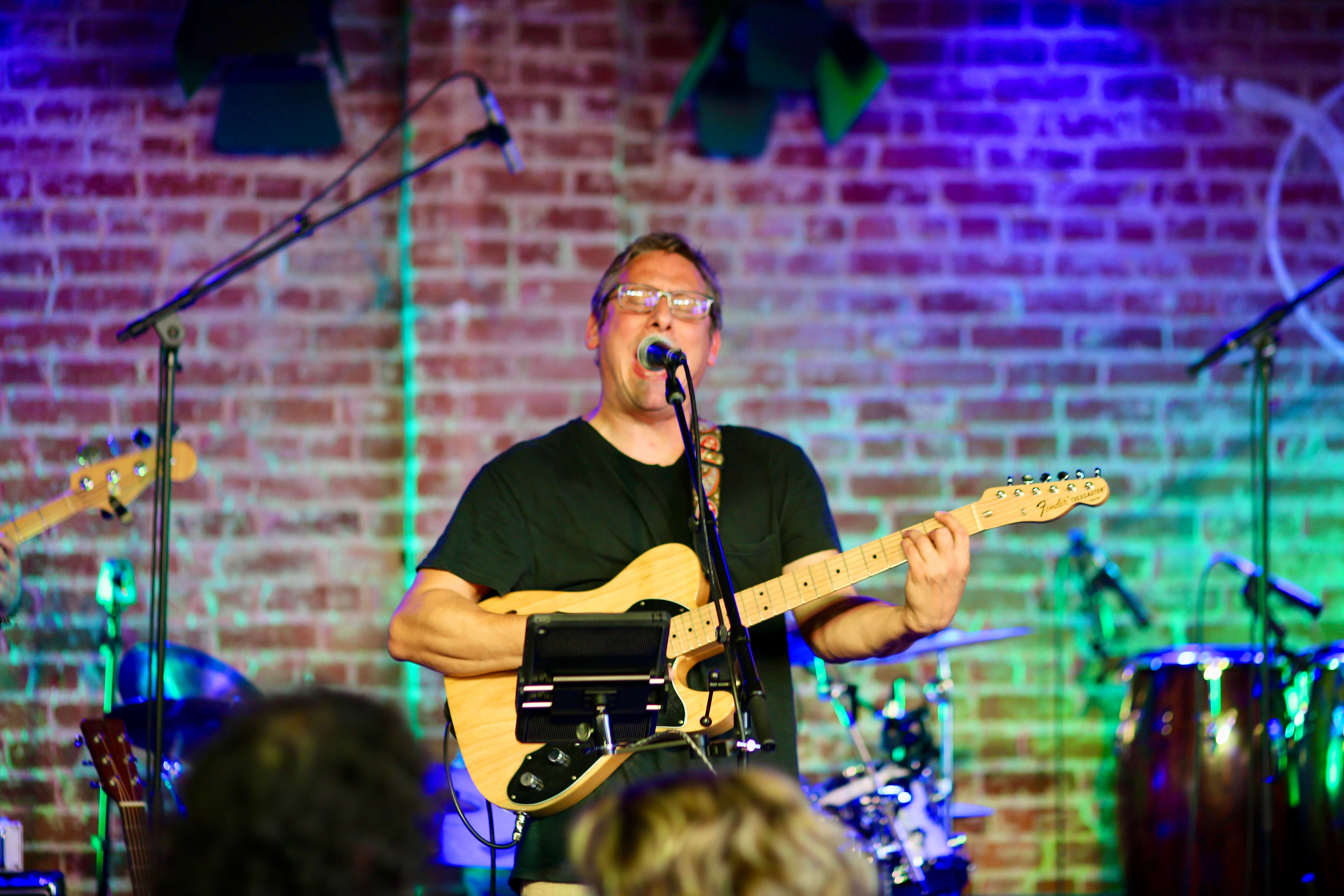 a man is playing a guitar in front of a brick wall