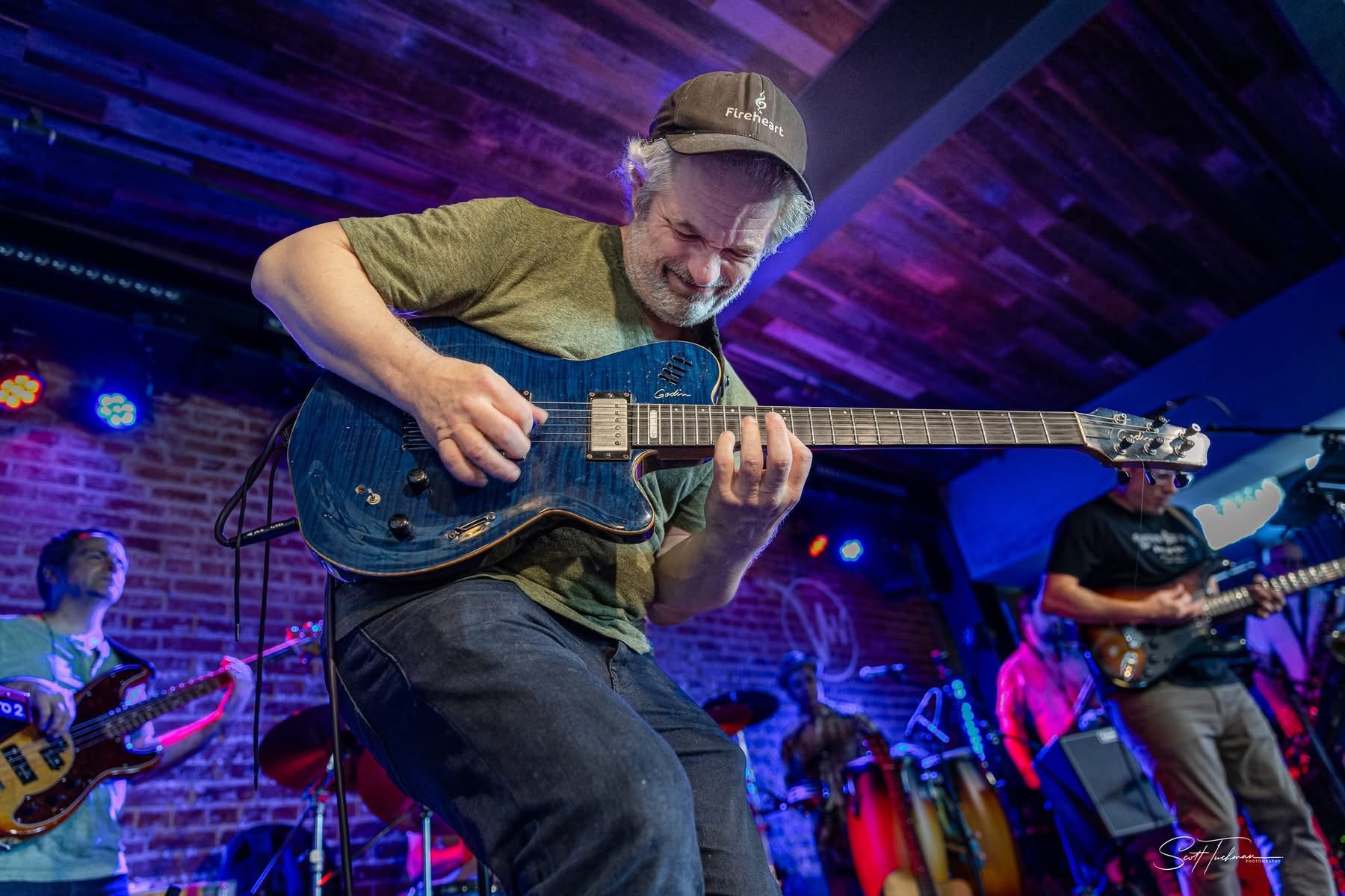 a man playing a guitar on stage in front of a brick wall