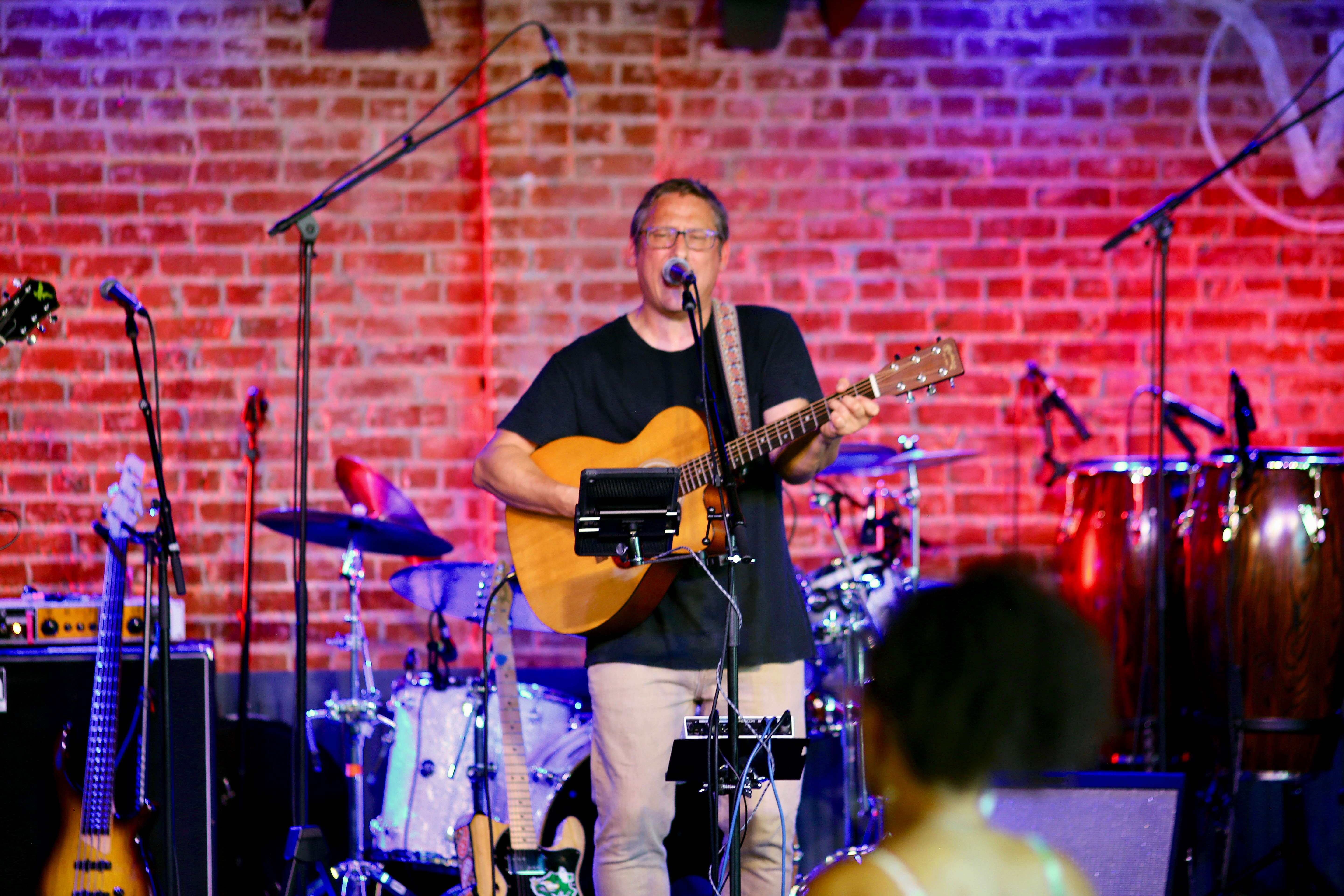 a man is playing an acoustic guitar in front of a brick wall