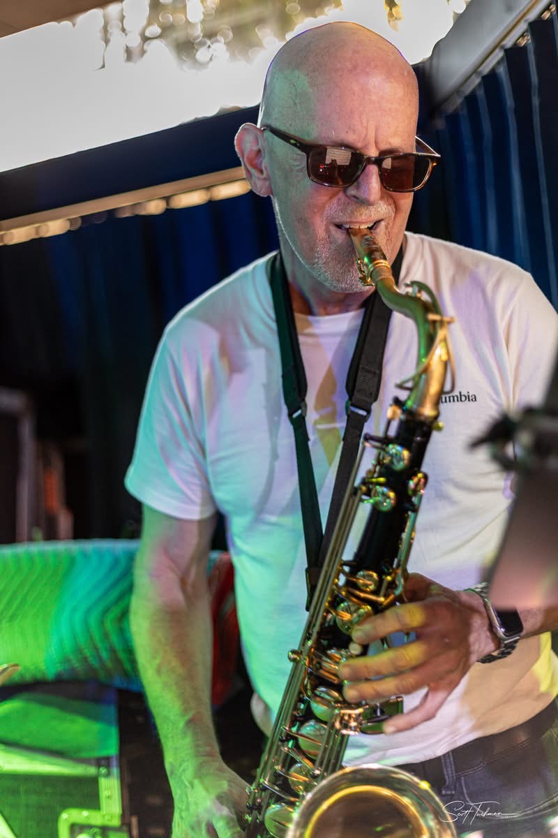 a bald man in sunglasses playing a saxophone
