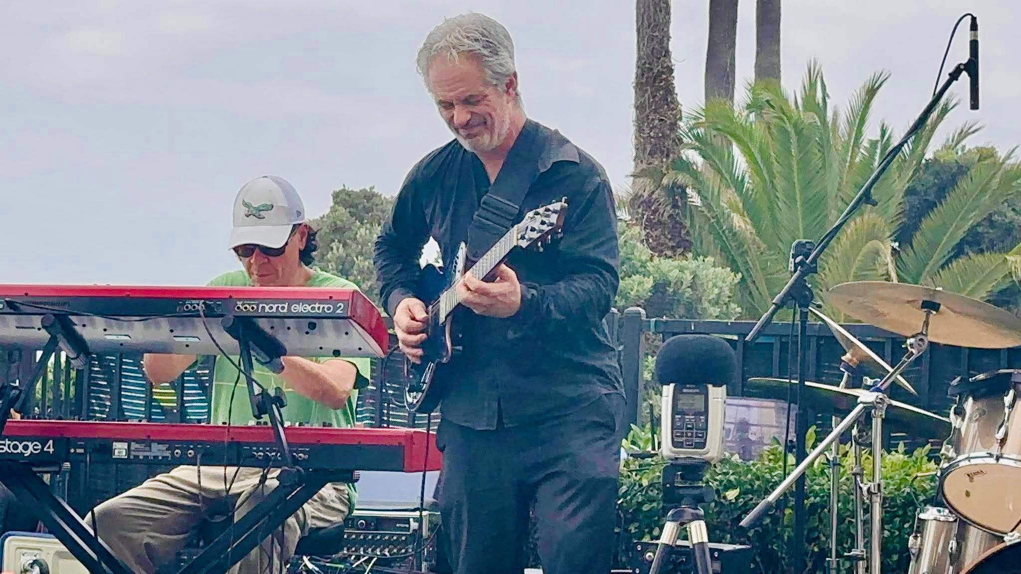 two men playing keyboards in front of a palm tree