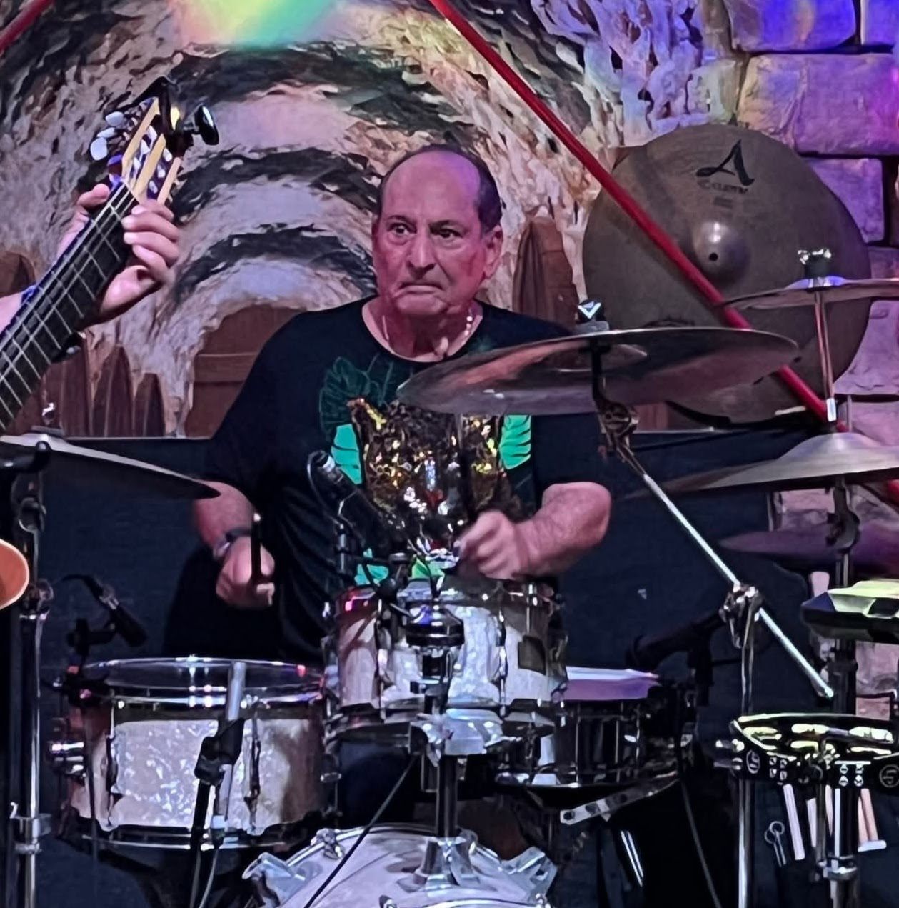 two men playing drums in front of a stone wall