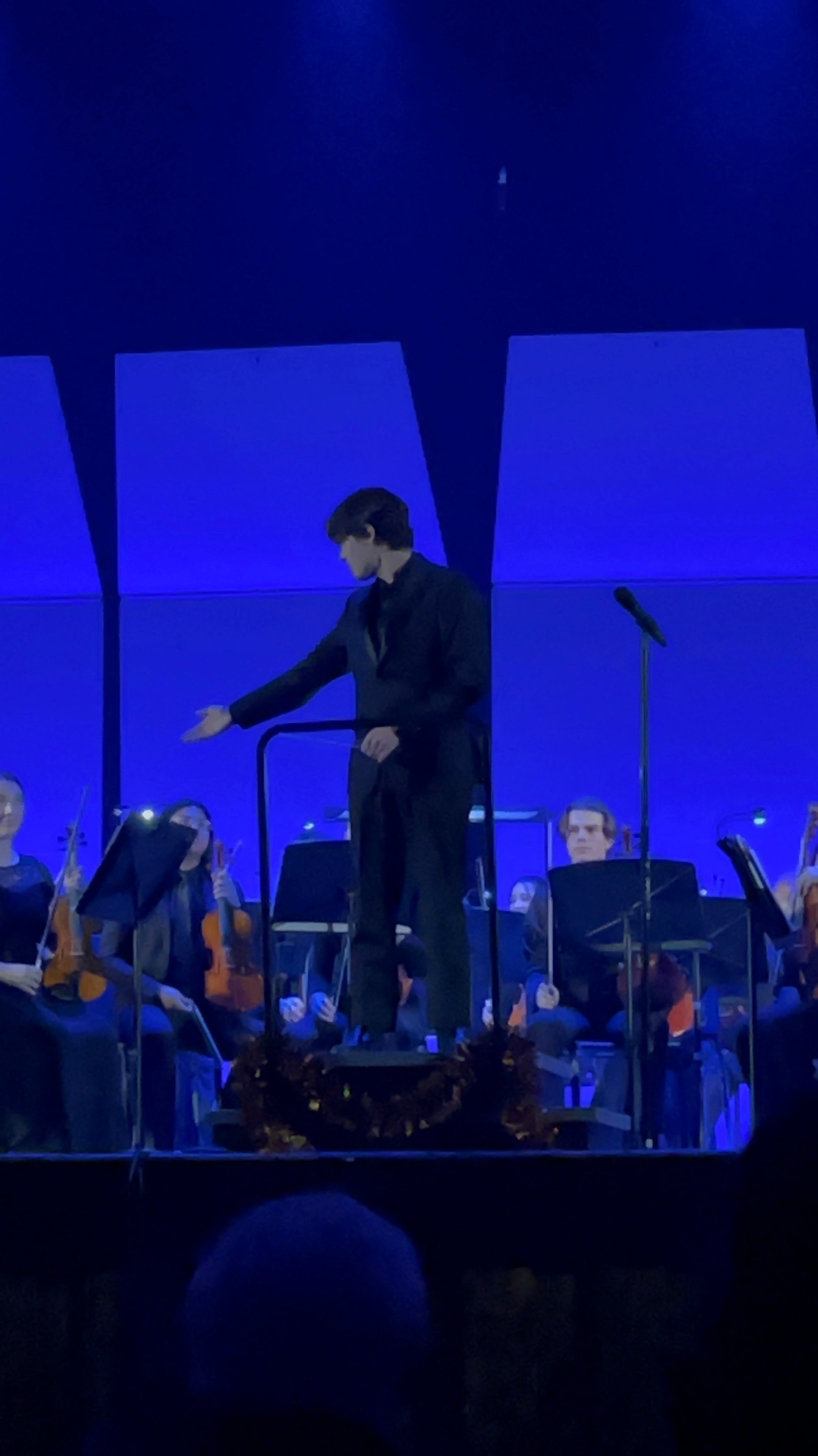 a man in a suit standing on stage with an orchestra