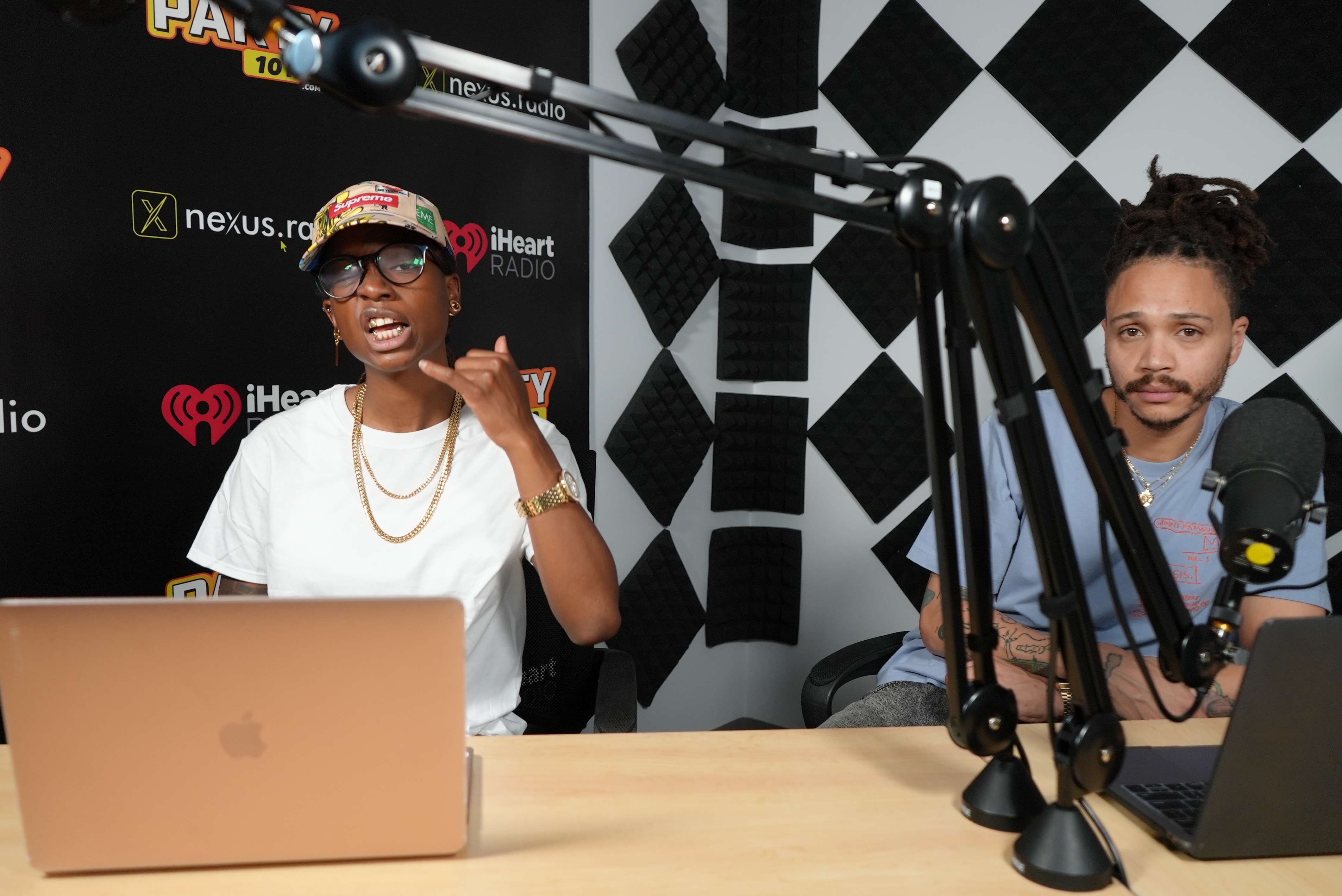 two people sitting at a desk with microphones and laptops