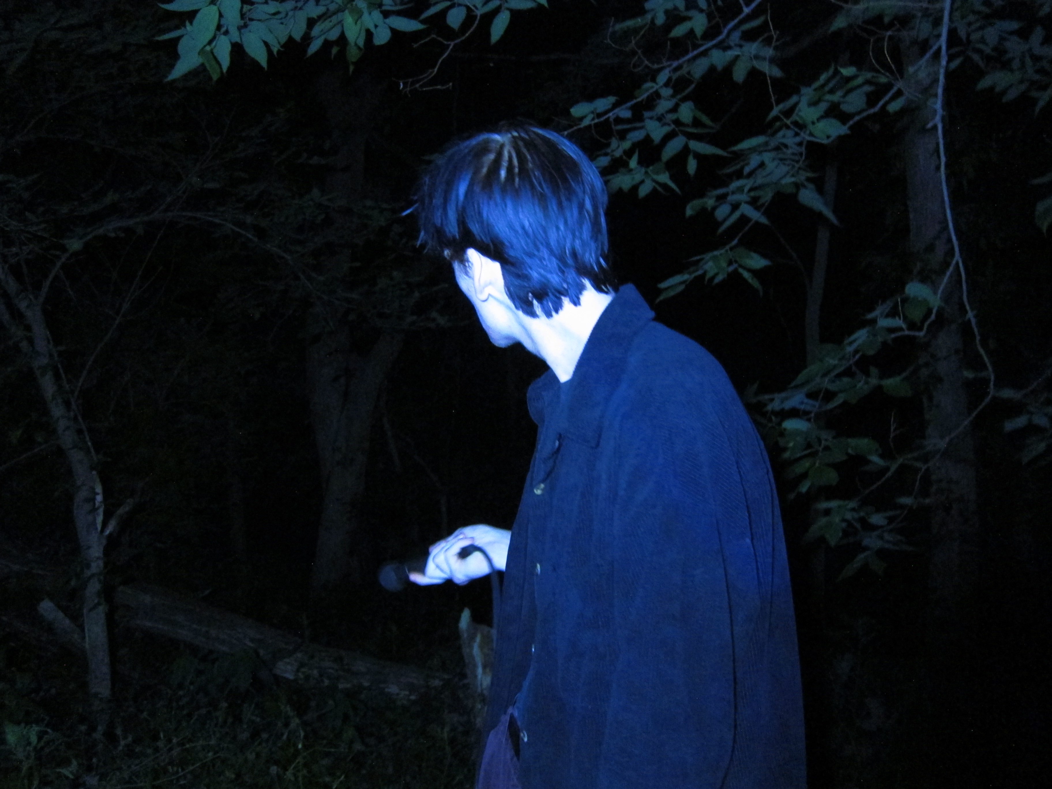 a man with blue hair standing in the woods at night