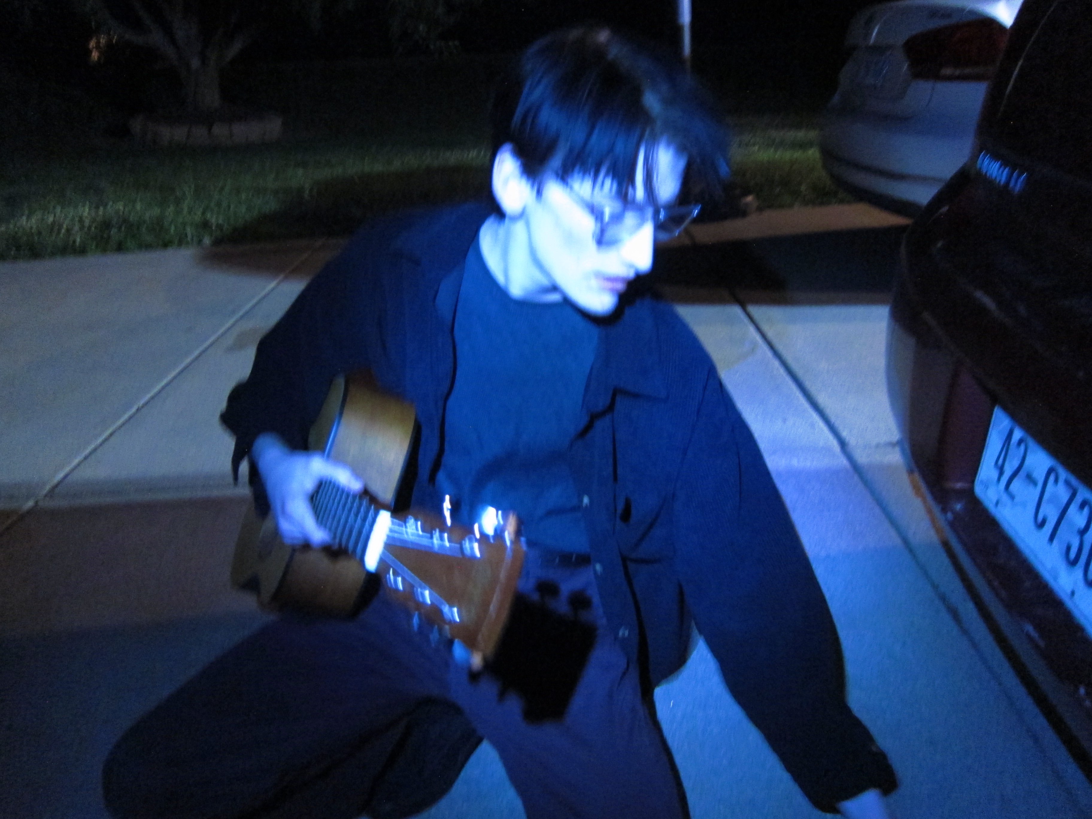 a man playing an acoustic guitar in front of a car