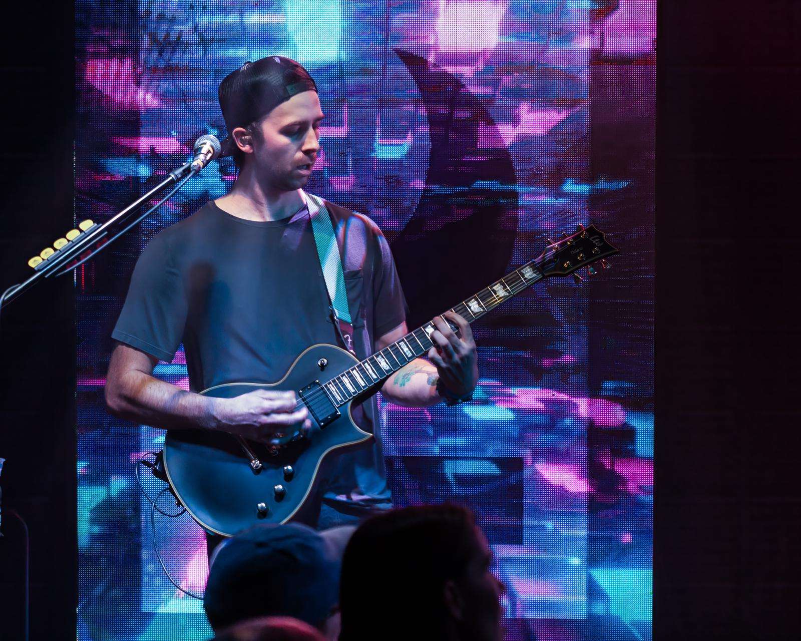 a man playing a guitar in front of a large screen