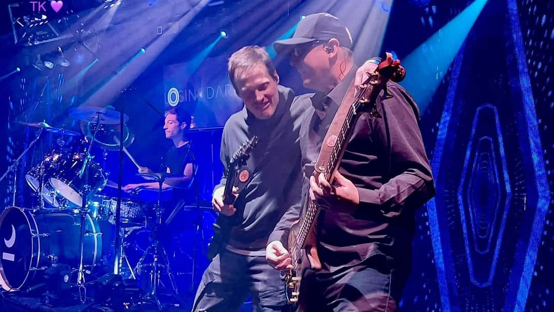 a group of men playing guitar on stage at a concert