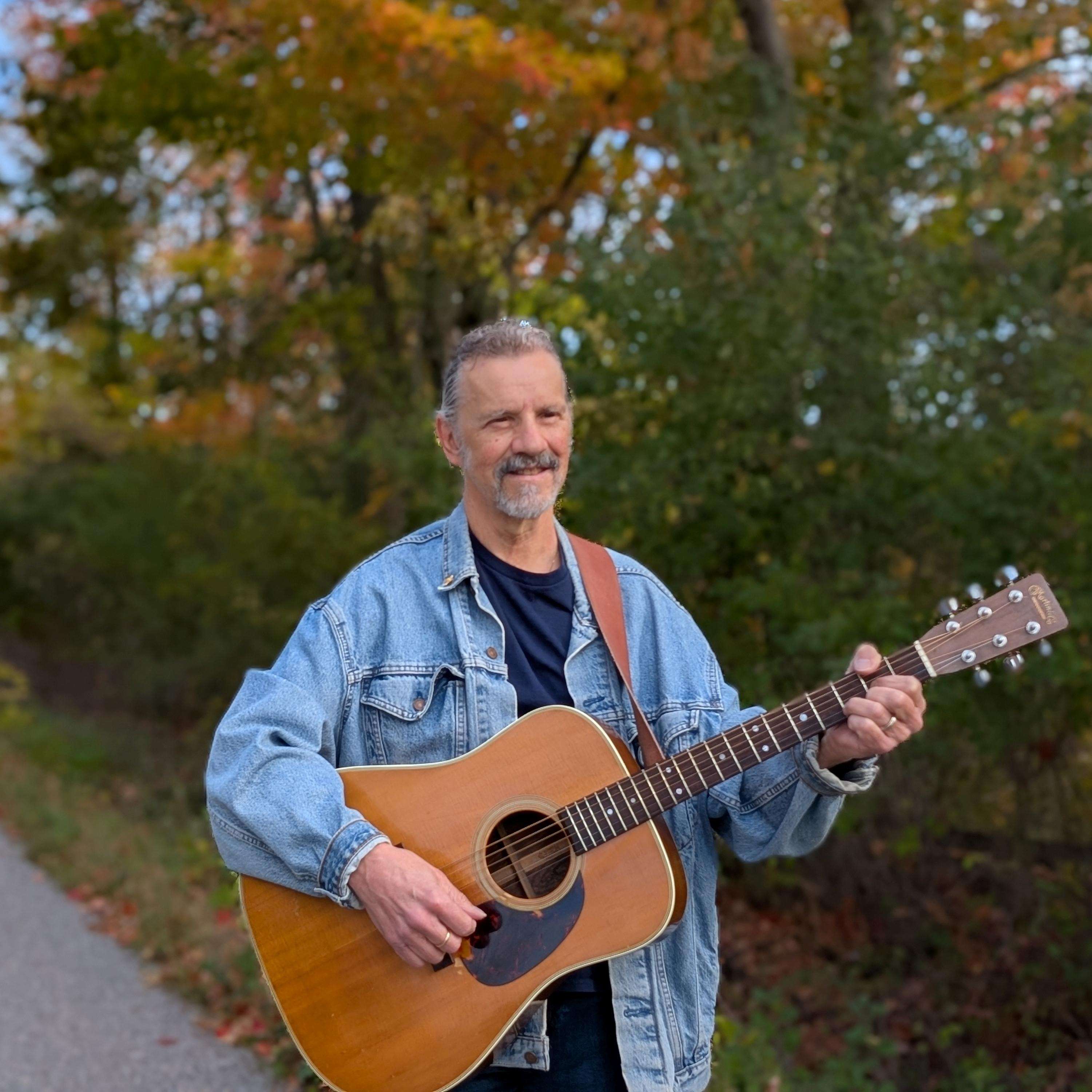 a man standing on a road with an acoustic guitar