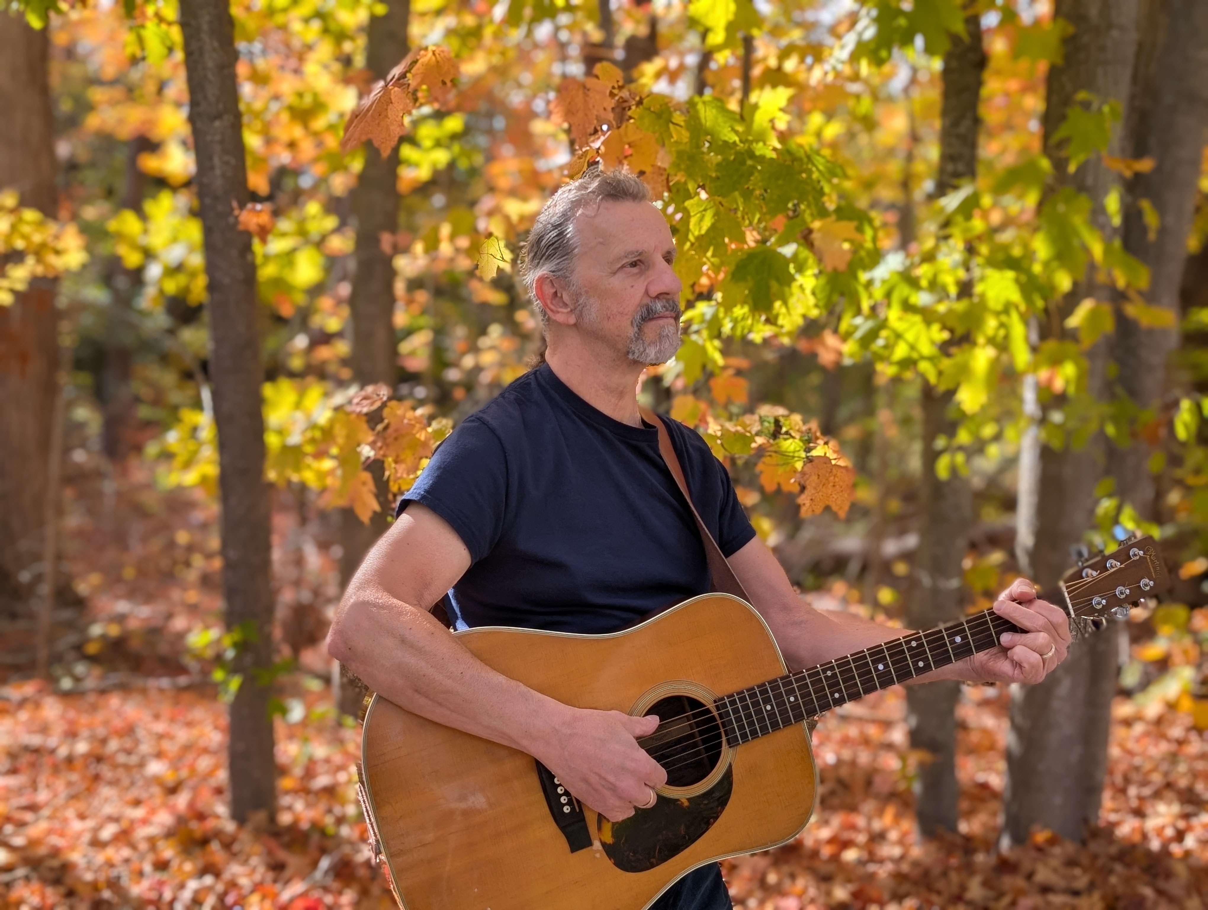 a man playing an acoustic guitar in the woods