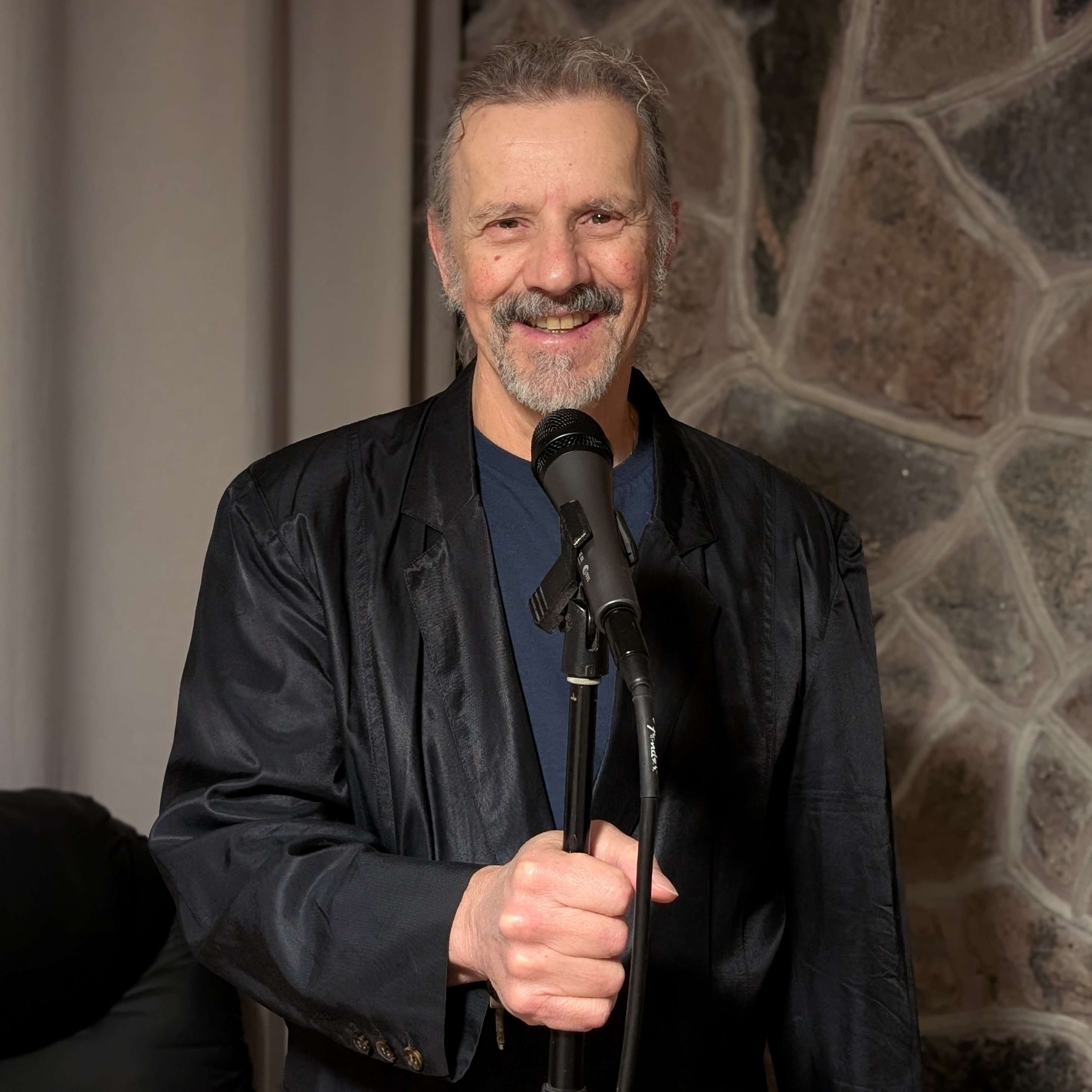 a man with a microphone standing in front of a stone wall