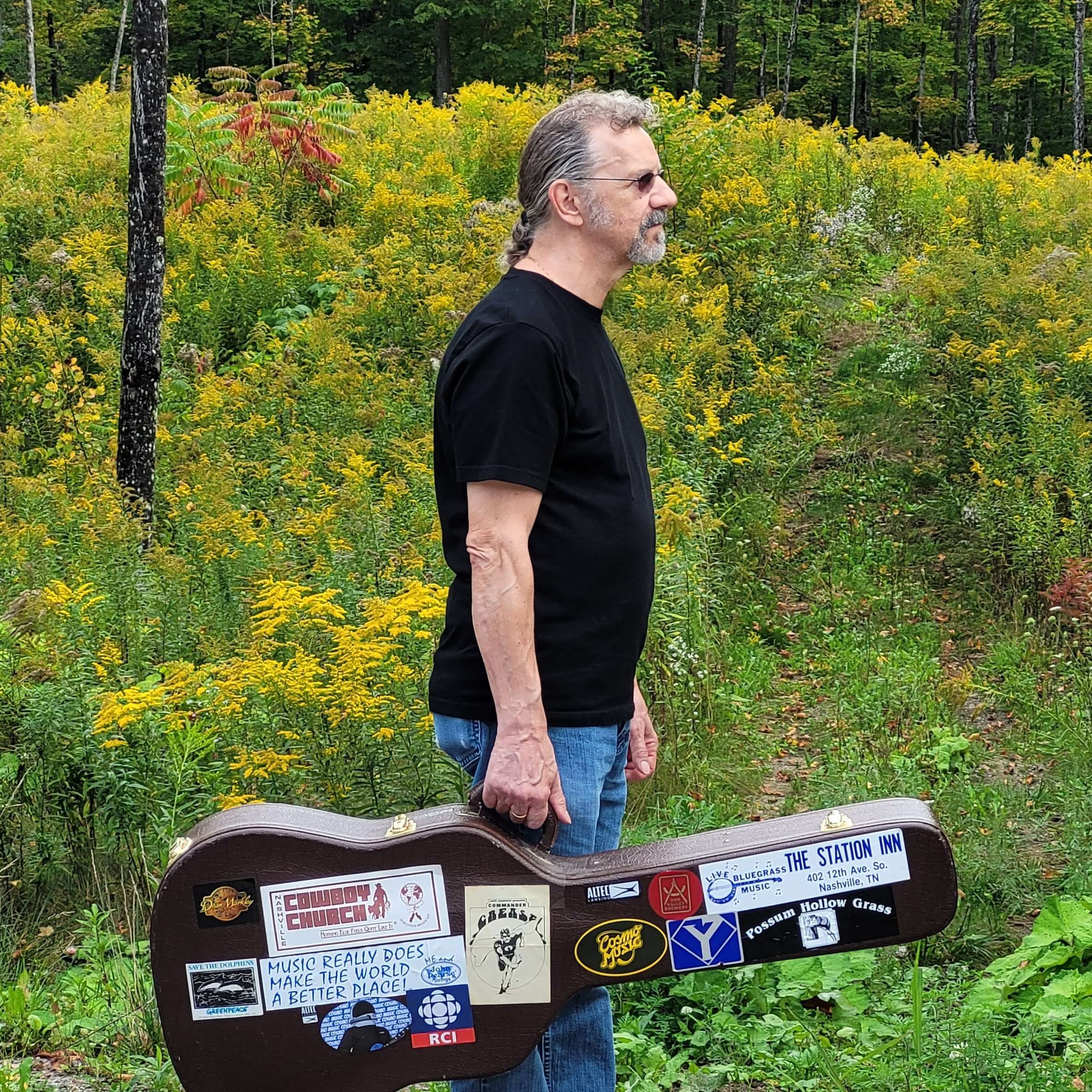 a man standing in the middle of a field with a guitar