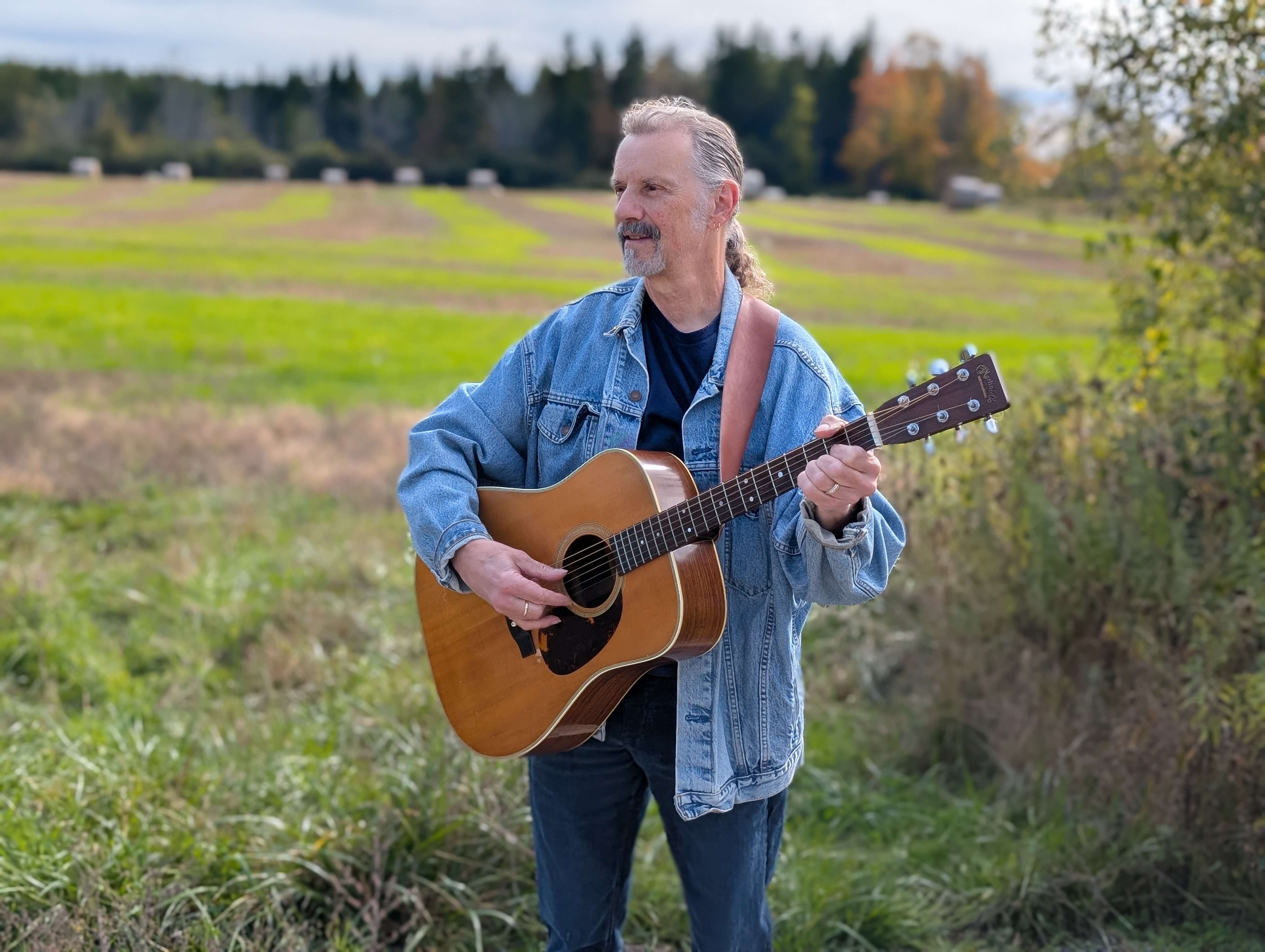 a man standing in a field with an acoustic guitar
