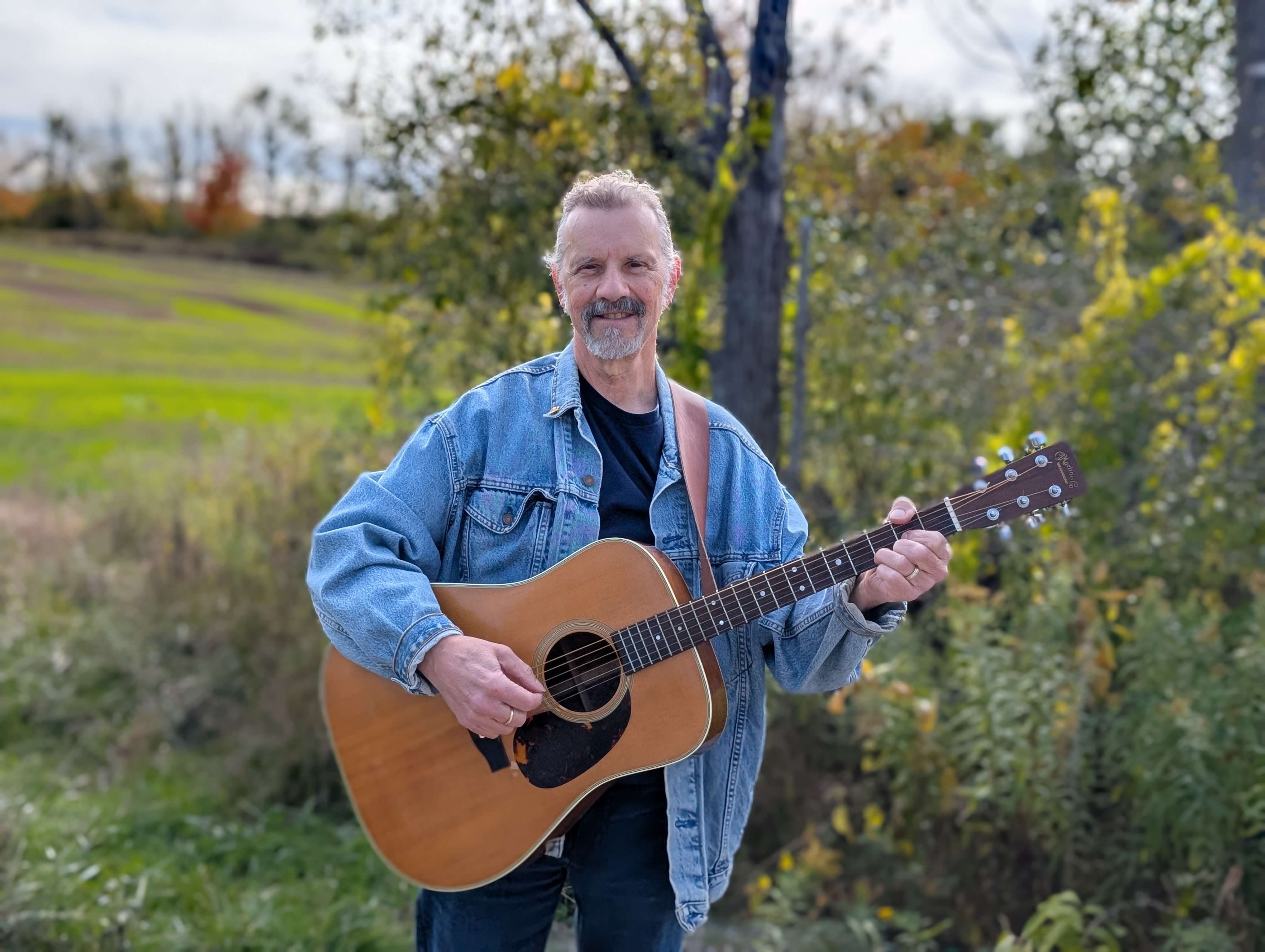 a man holding an acoustic guitar in a field