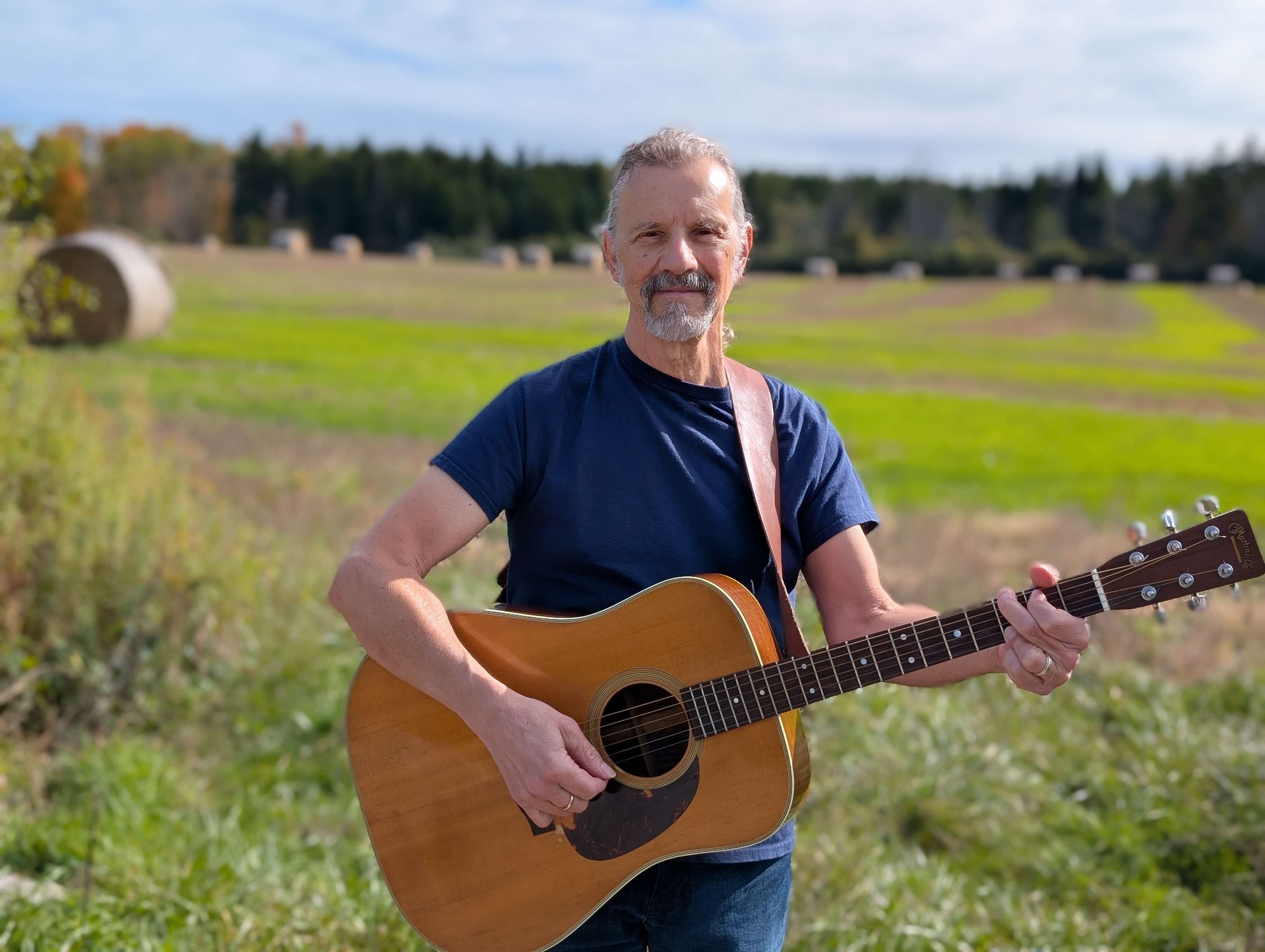 a man holding an acoustic guitar in a field