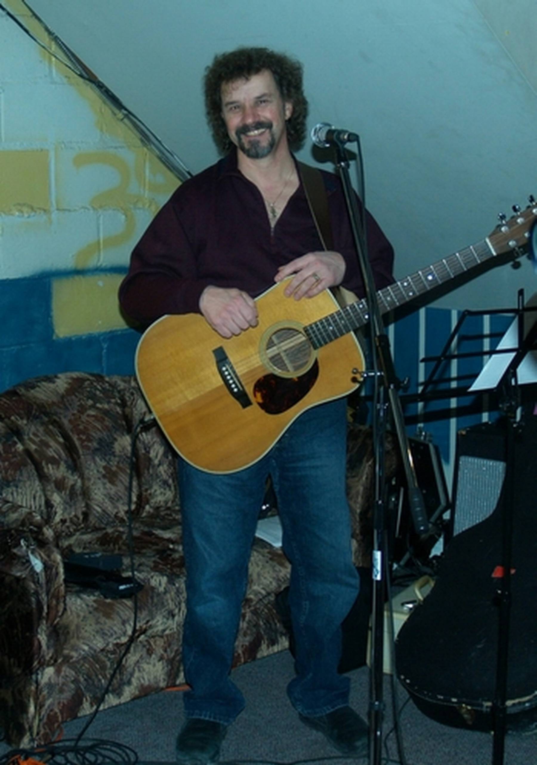 a man holding an acoustic guitar in front of a microphone