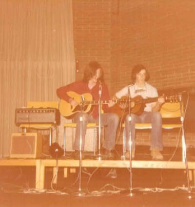 two men sitting on a stage with guitars
