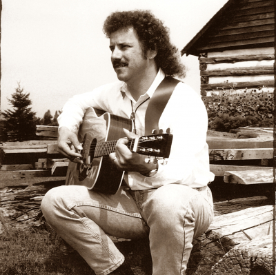 a man sitting on a wooden bench with an acoustic guitar