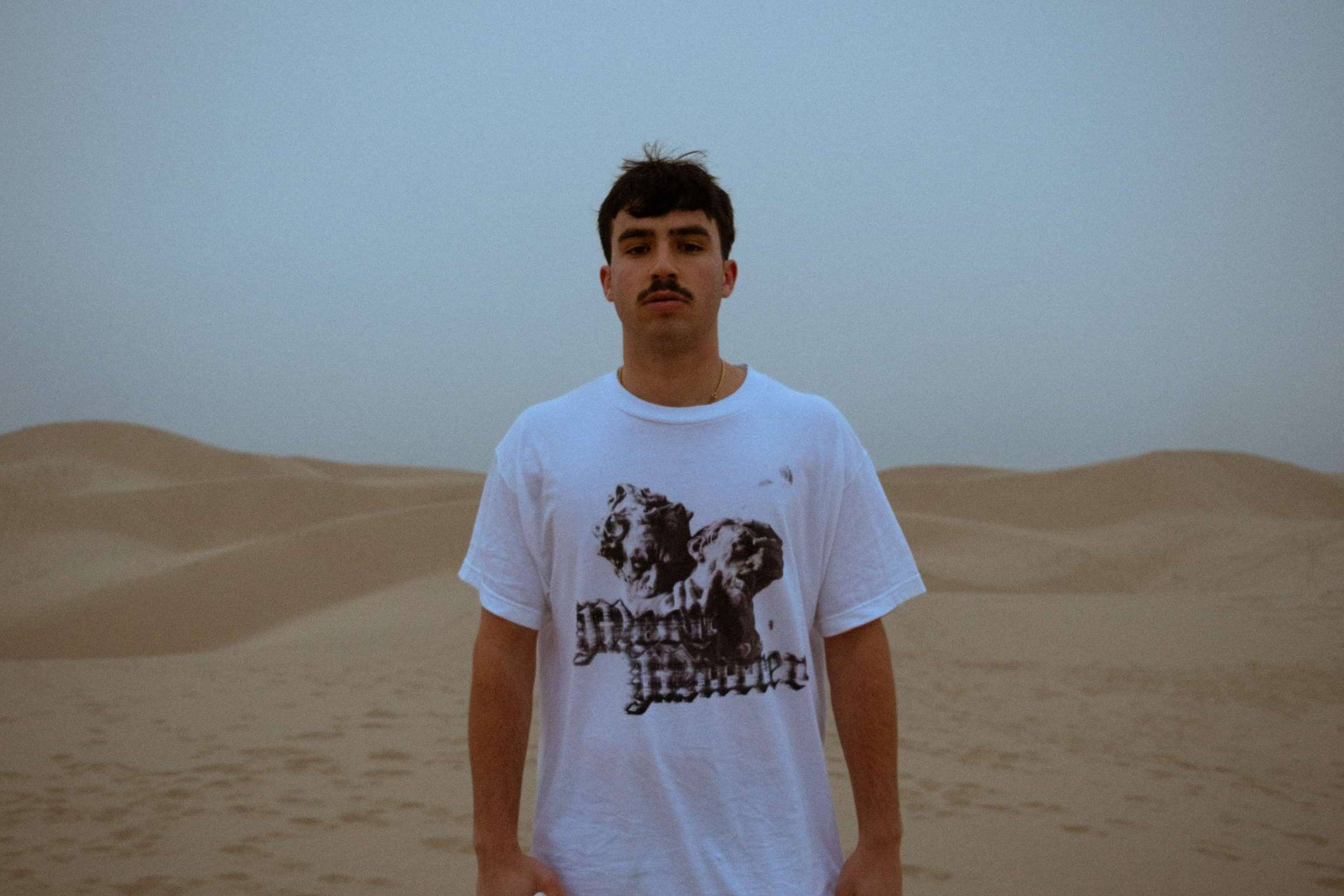 a man in a white t - shirt standing in the desert
