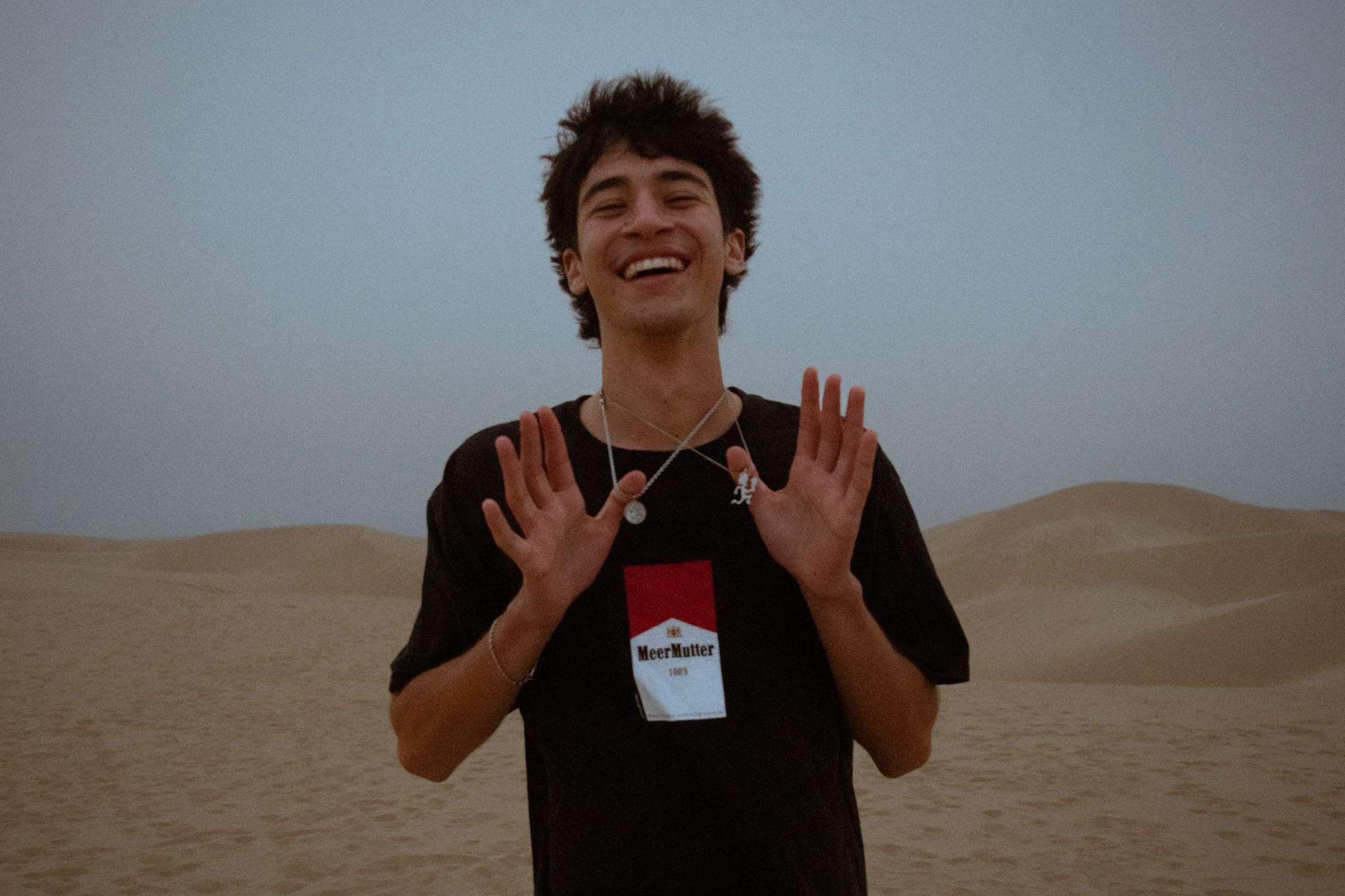 a young man standing in the desert with his hands up