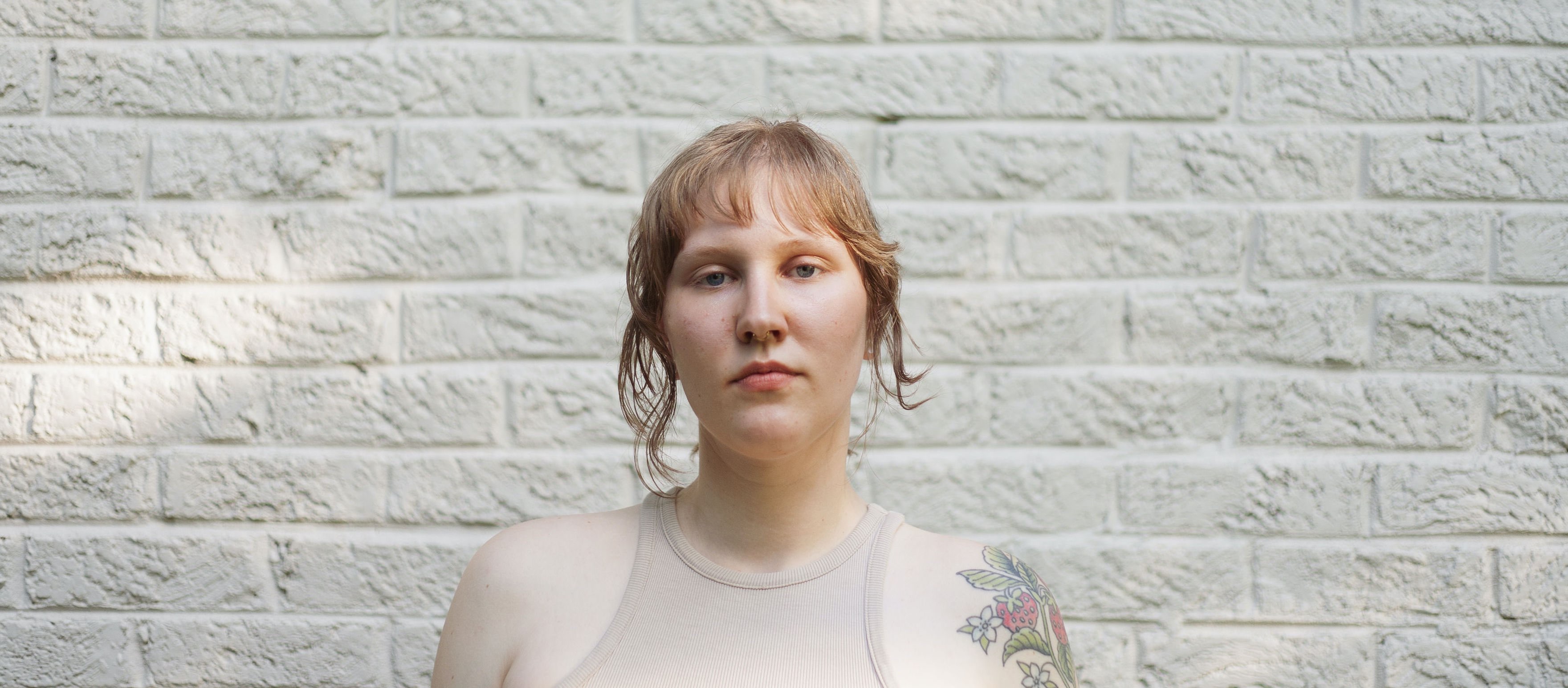 a woman with tattoos standing in front of a white brick wall